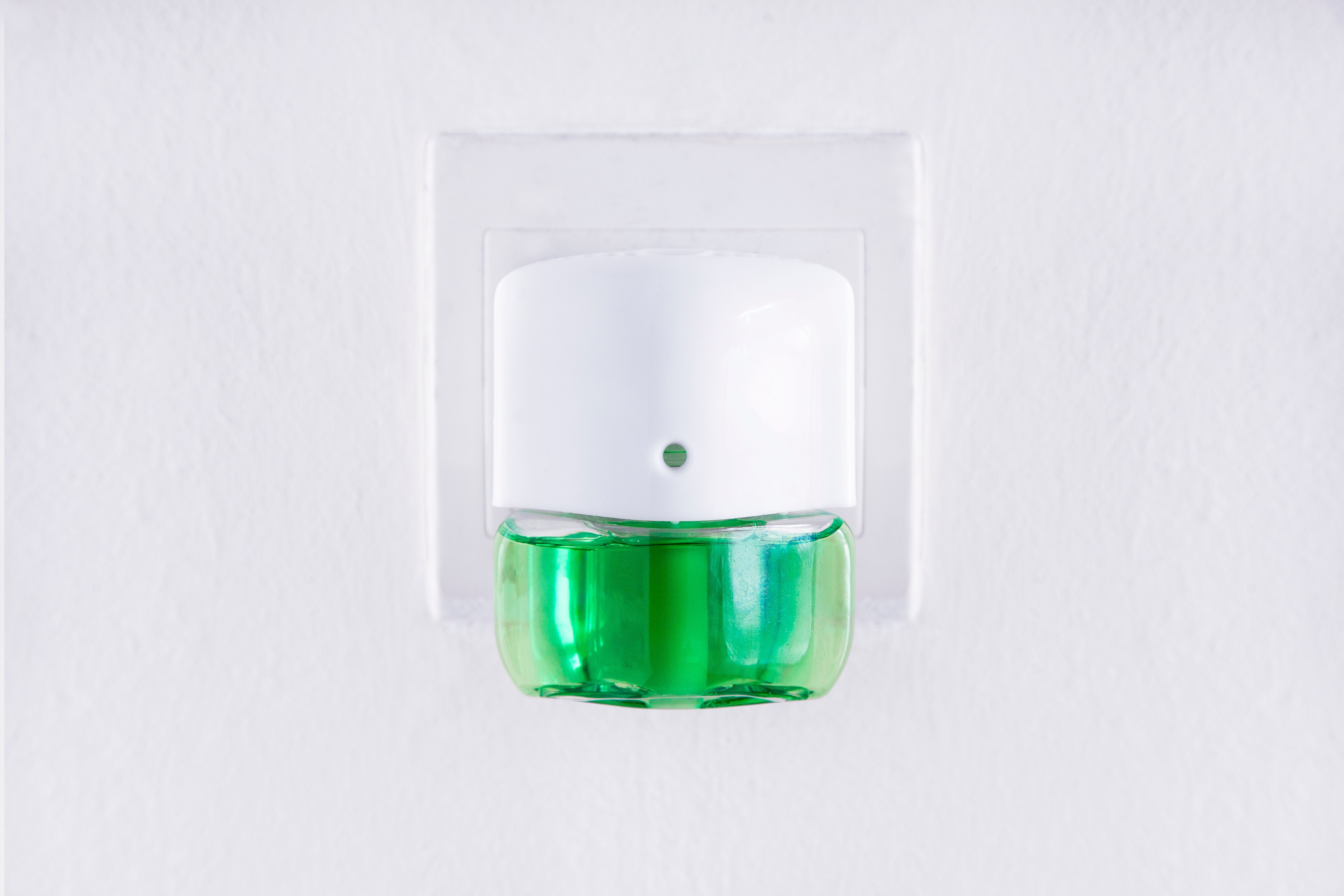 Wall-mounted aerial  freshener plugged into an outlet with a greenish  refill bottle