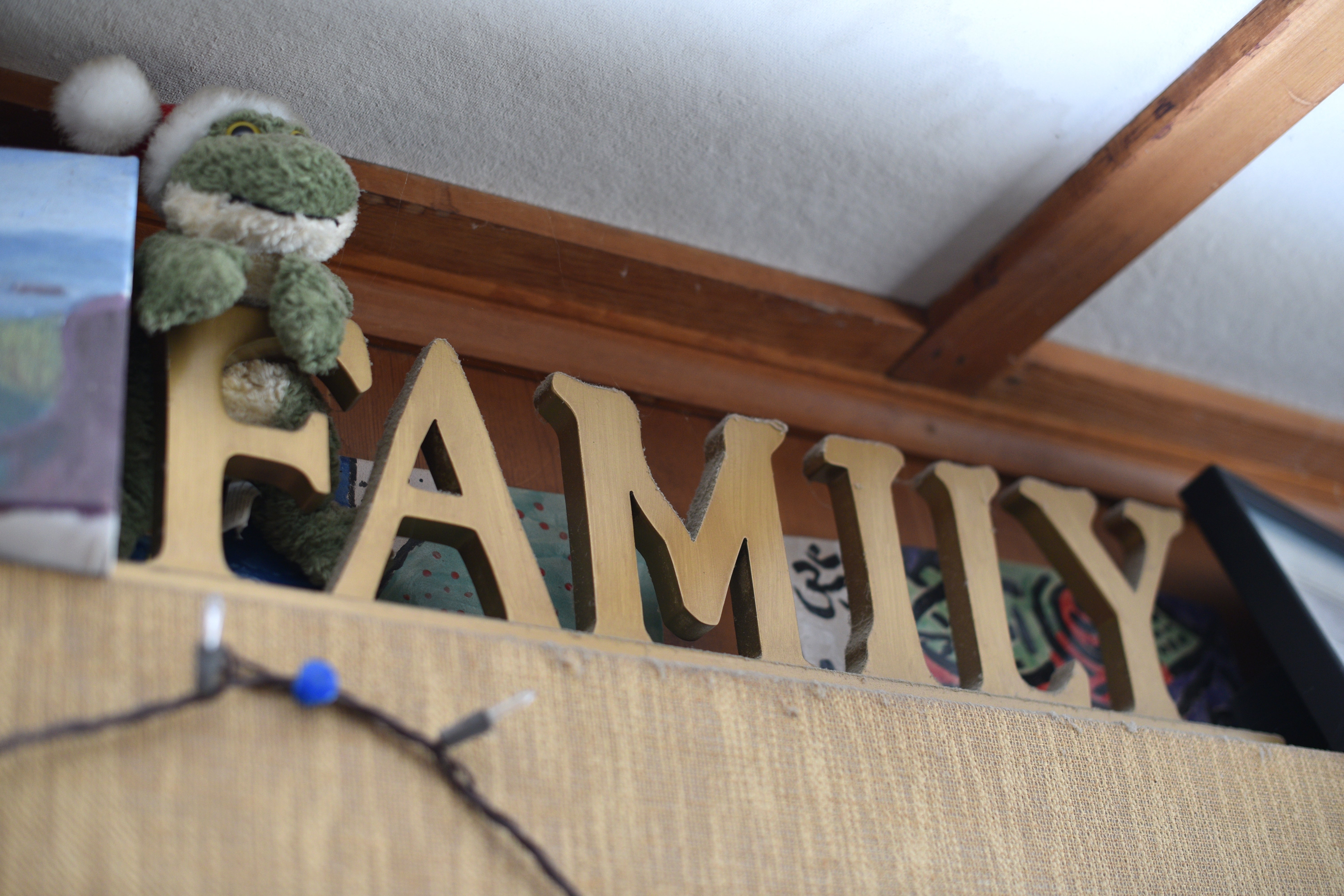 Gold letters spell "FAMILY" connected  a support  with a plush frog wearing a Santa chapeau  adjacent  to it