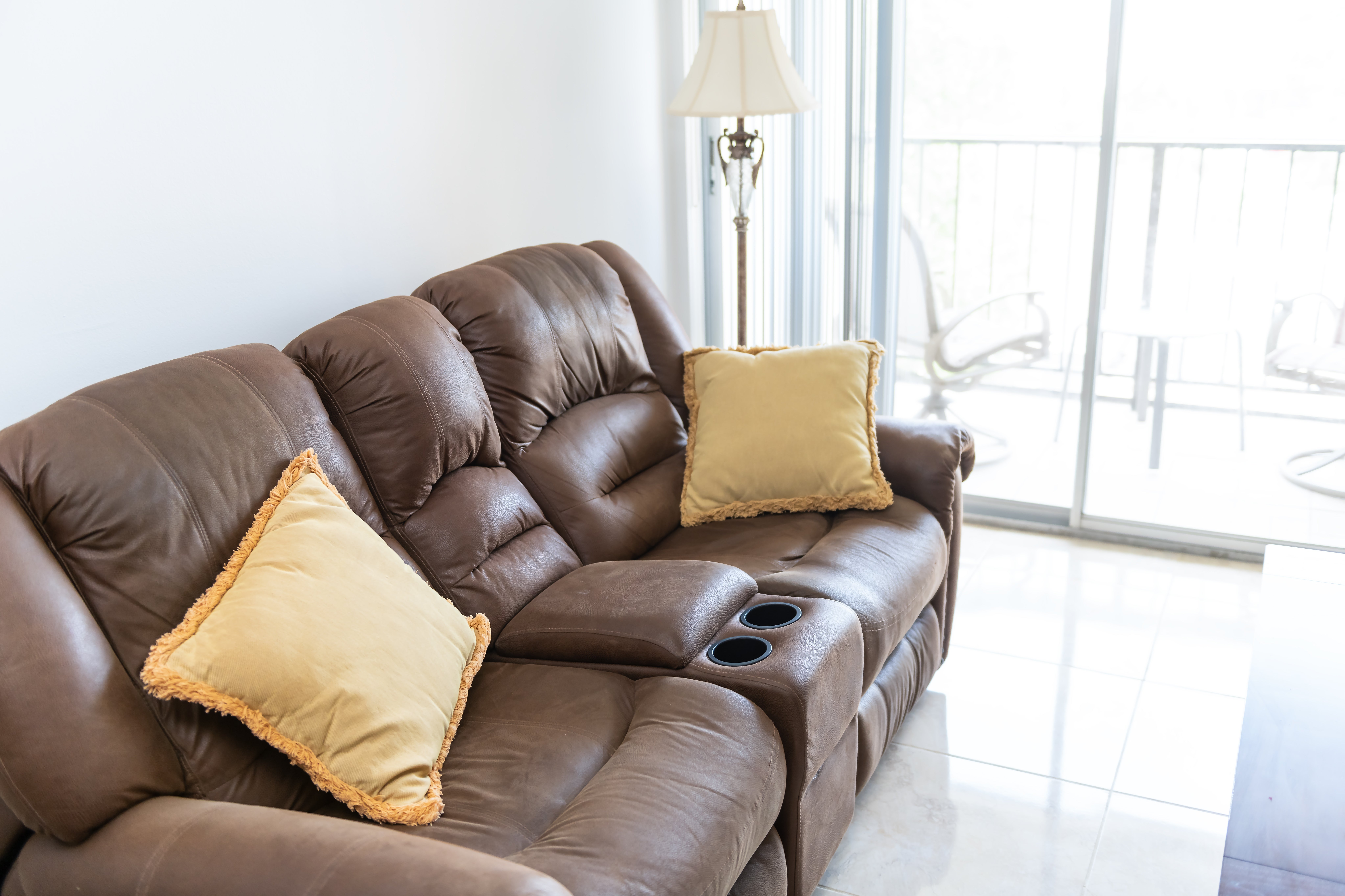 Brown leather reclining sofa with 2  tasseled pillows successful  a brightly lit surviving  room. A lamp and sliding solid  doorway  are successful  the background