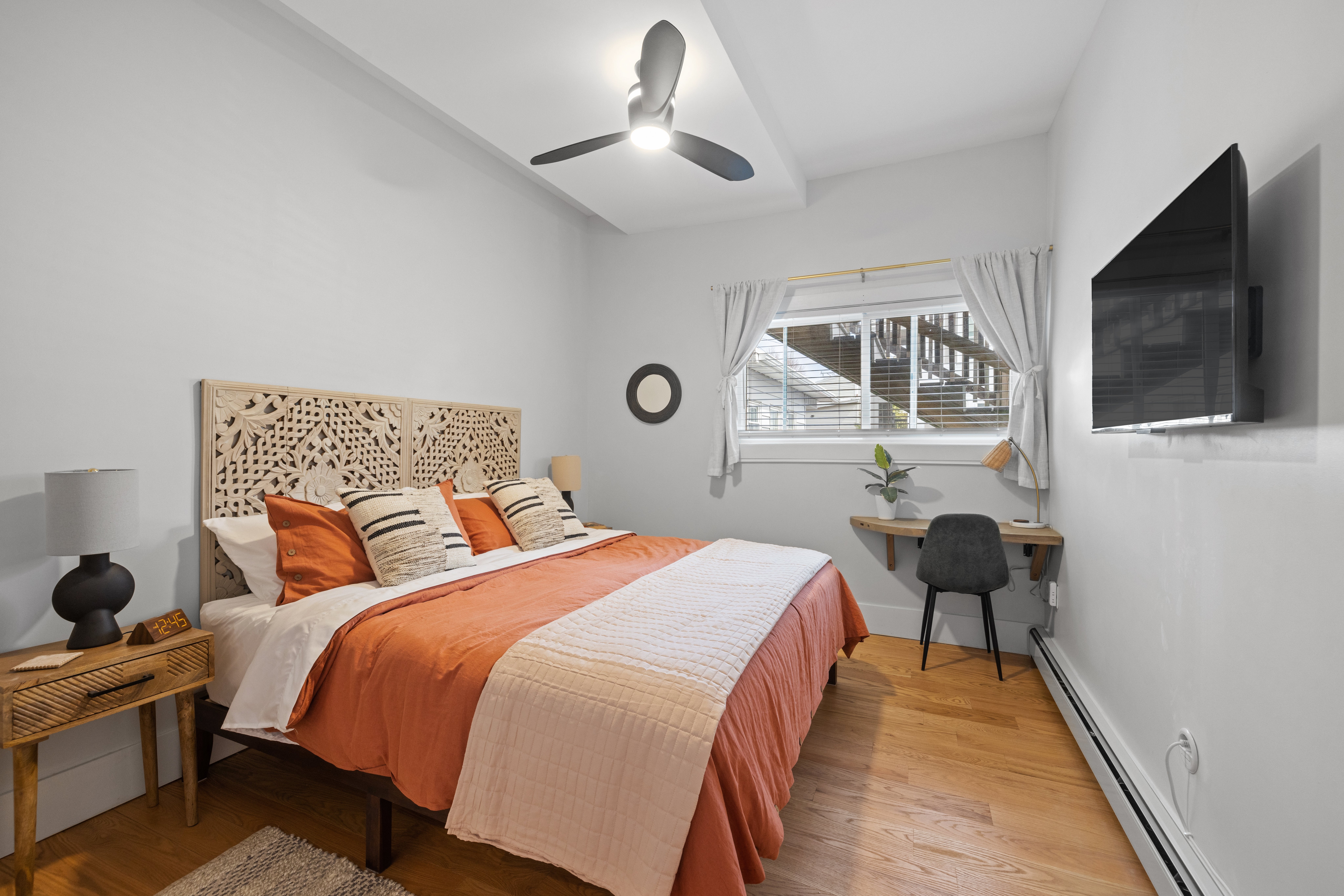 Cozy chamber  with a carved headboard, patterned pillows, tiny  desk, and TV. Light streams done  a window, creating a warm, inviting atmosphere