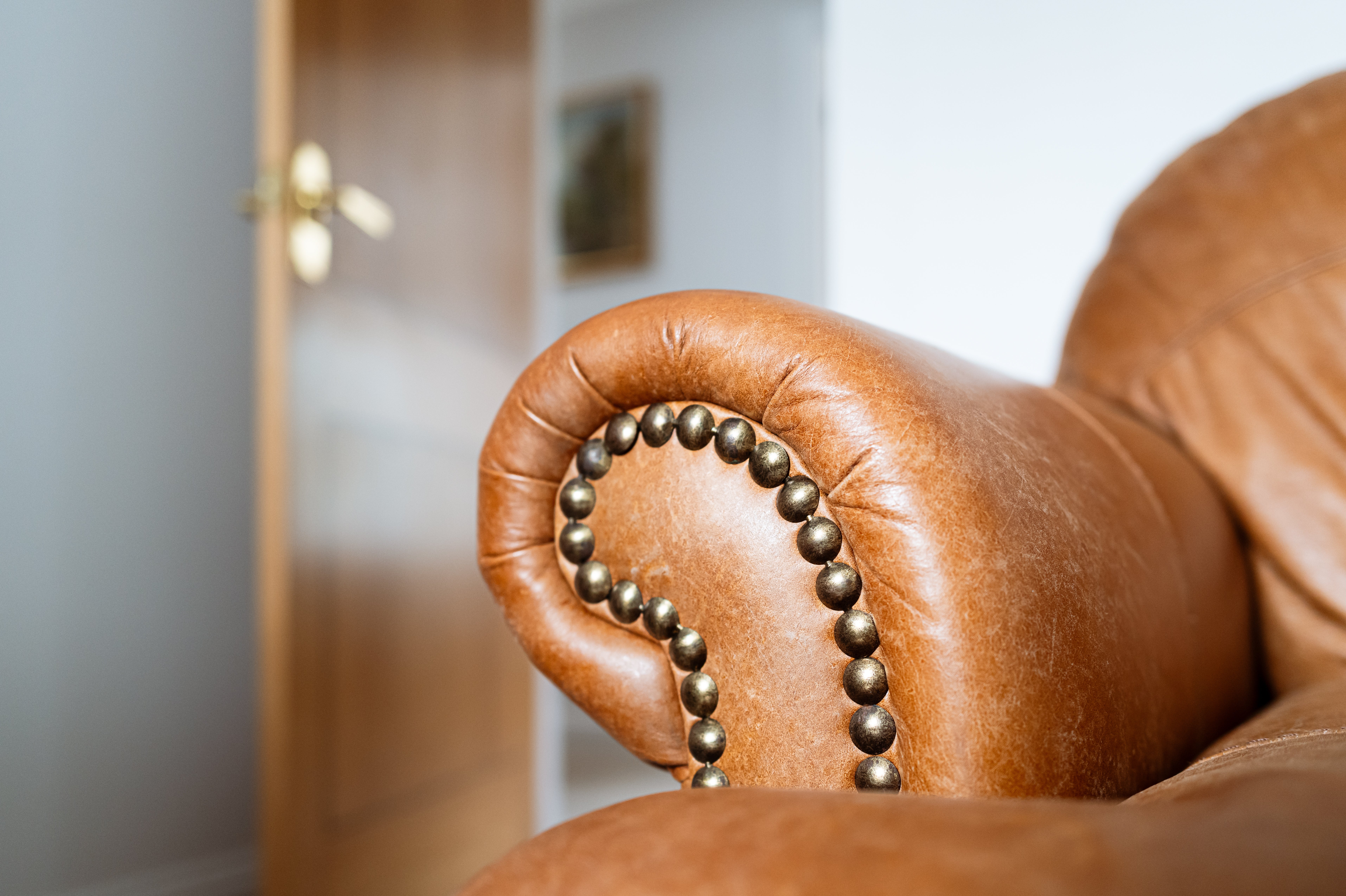 Close-up of a leather sofa armrest with metallic stud detailing successful  a surviving  country   setting. Door somewhat  ajar successful  the background