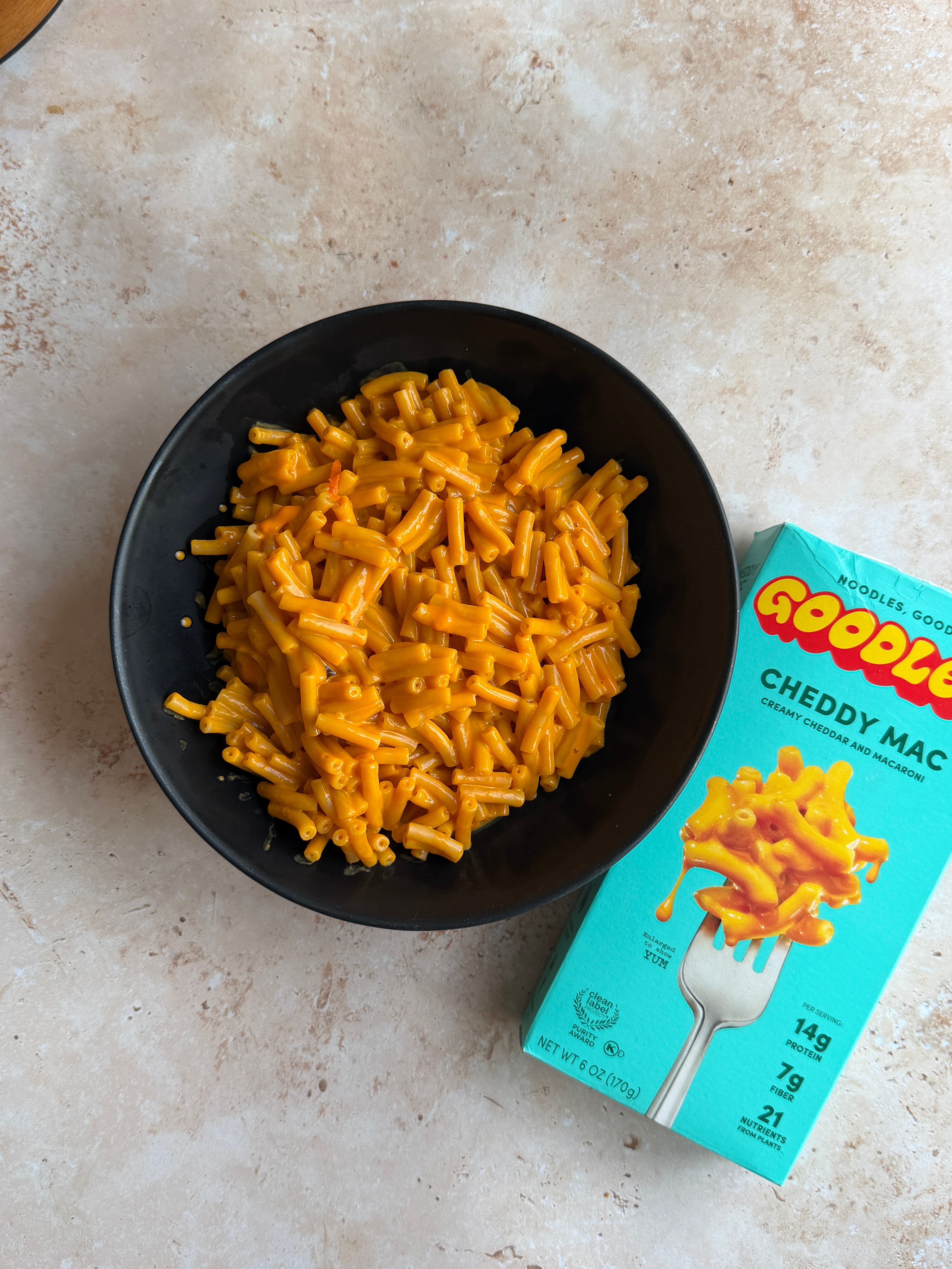 Bowl of cooked macaroni and cheese beside a box labeled "Goodles Cheddy Mac."