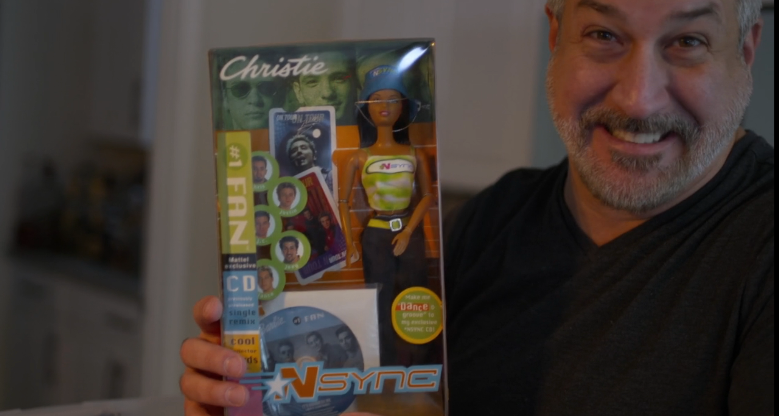 Person smiling portion holding an NSYNC-themed Barbie doll container featuring a doll and CD