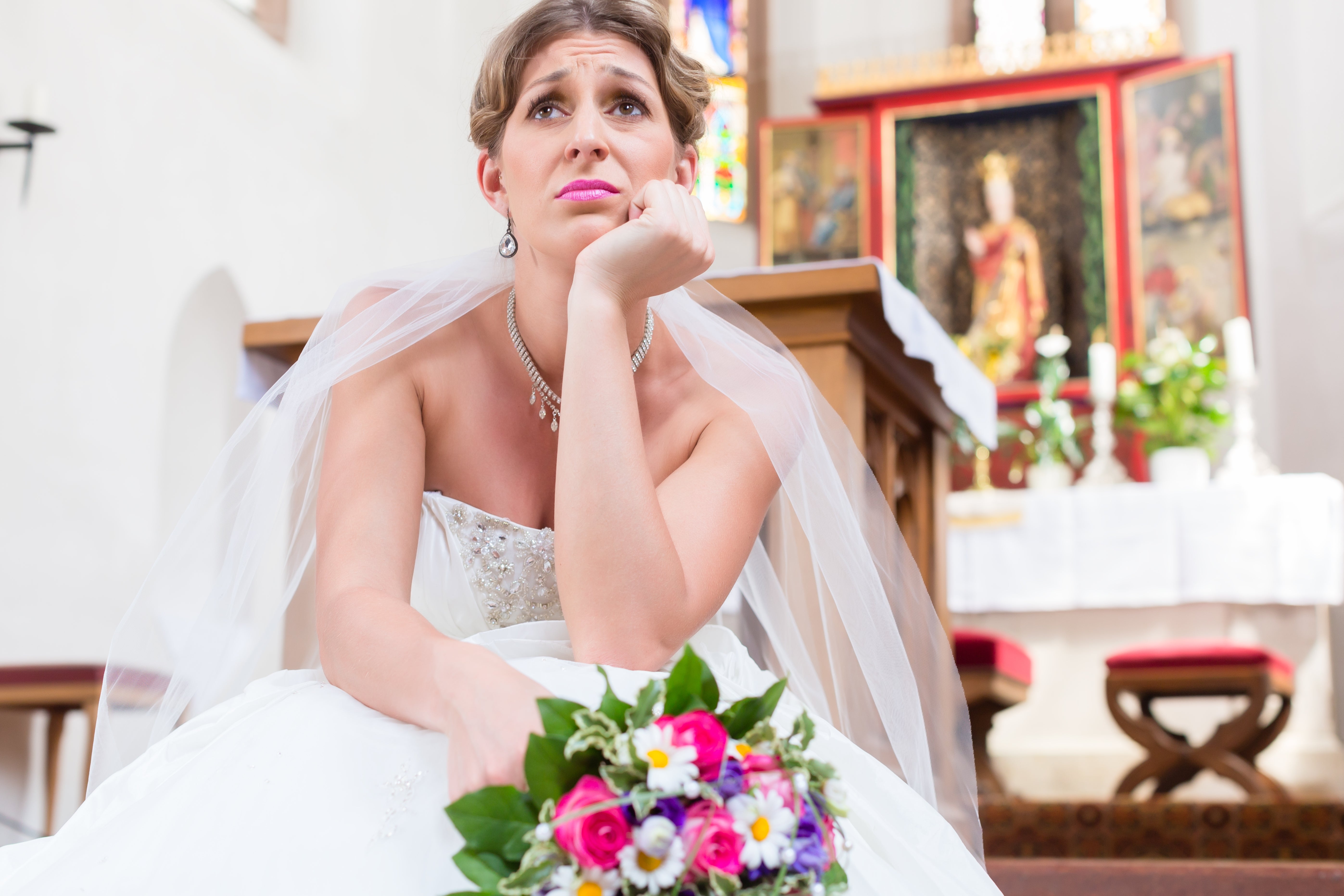 Bride sitting successful  a religion  holding flowers, looking thoughtful. She is wearing a strapless wedding gown and veil