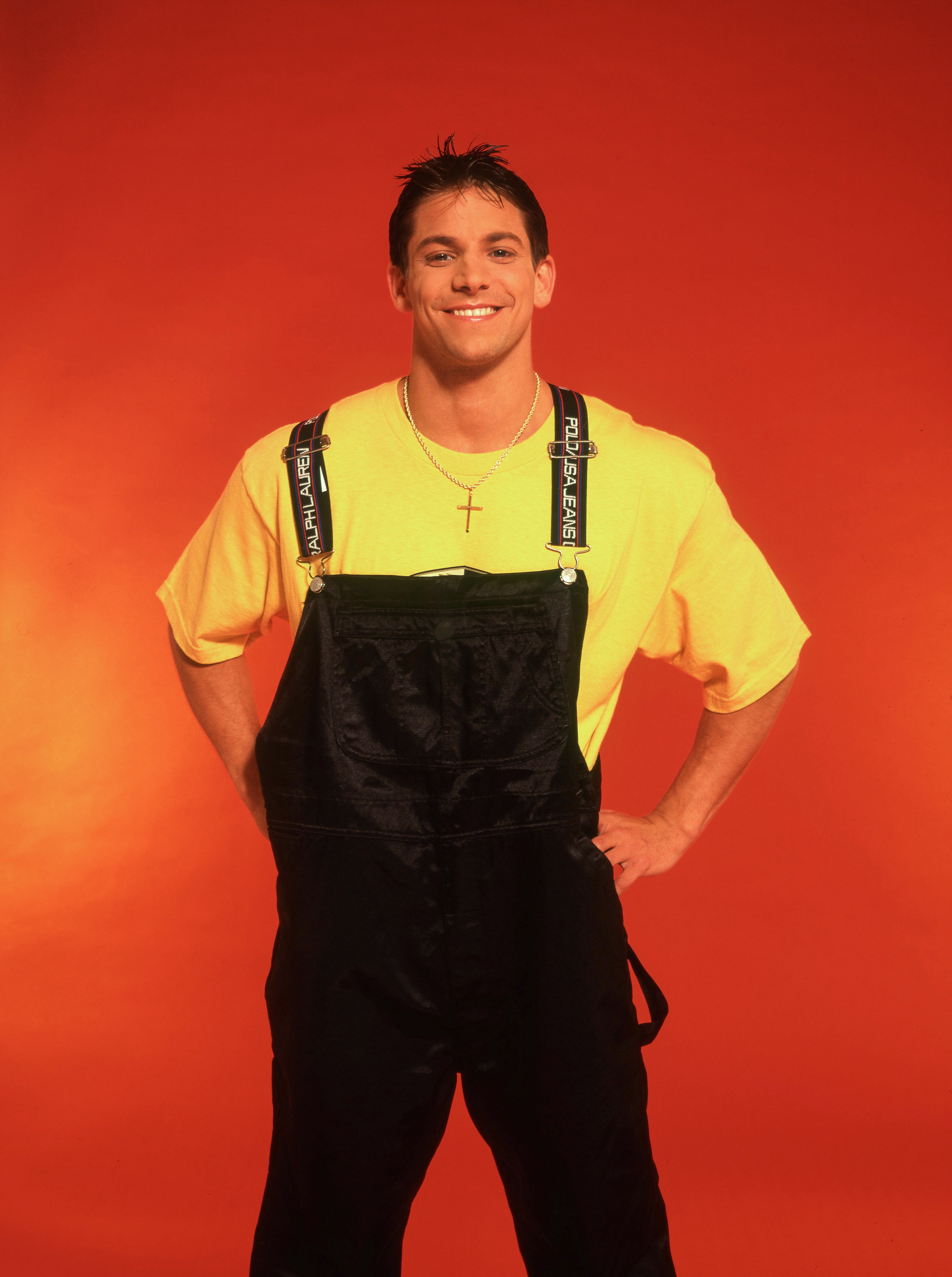Person wearing a agleam t-shirt with overalls, lasting confidently against a plain backdrop