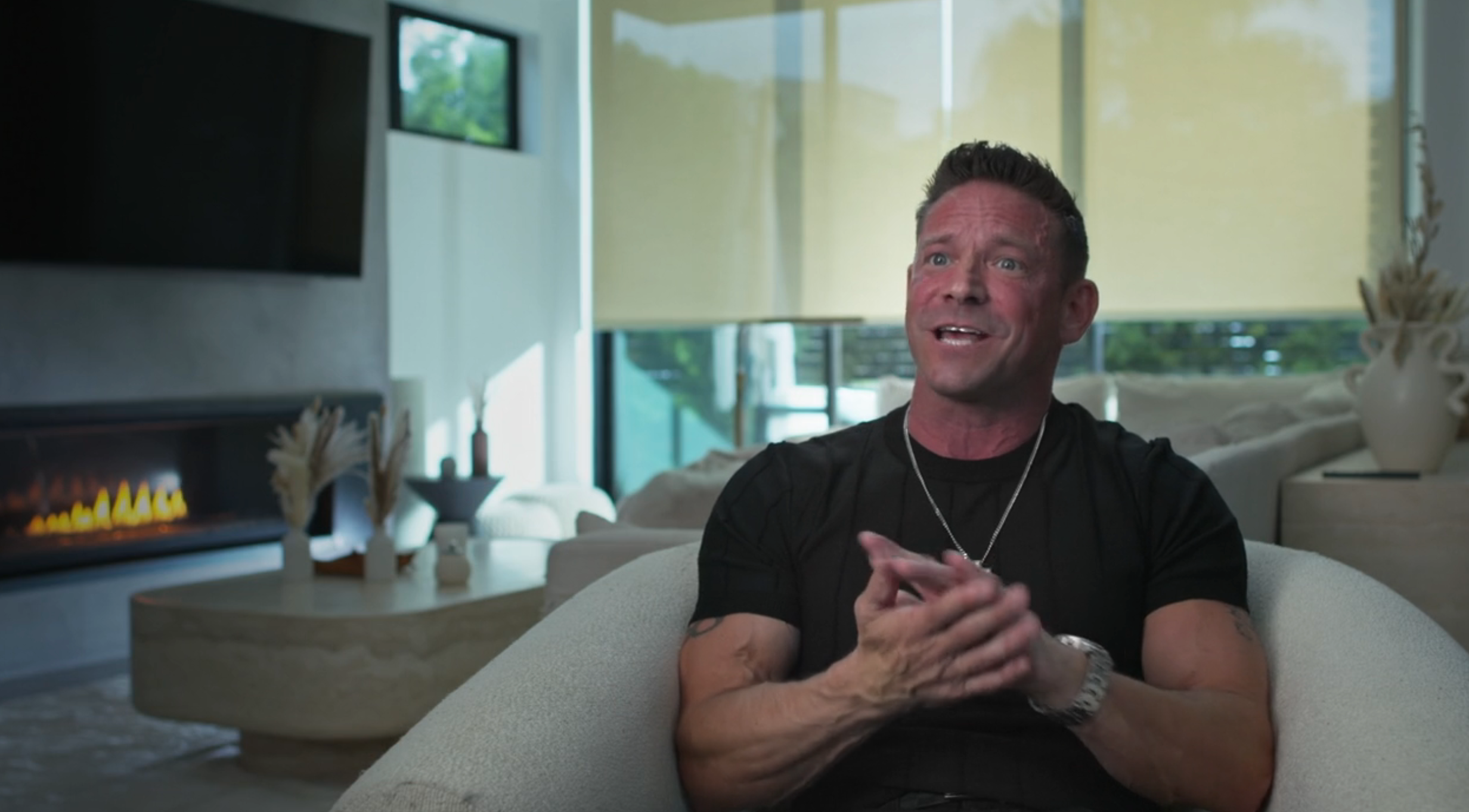 Person successful a modern surviving room, sitting connected a couch, casually dressed and speaking, with a fireplace successful the background