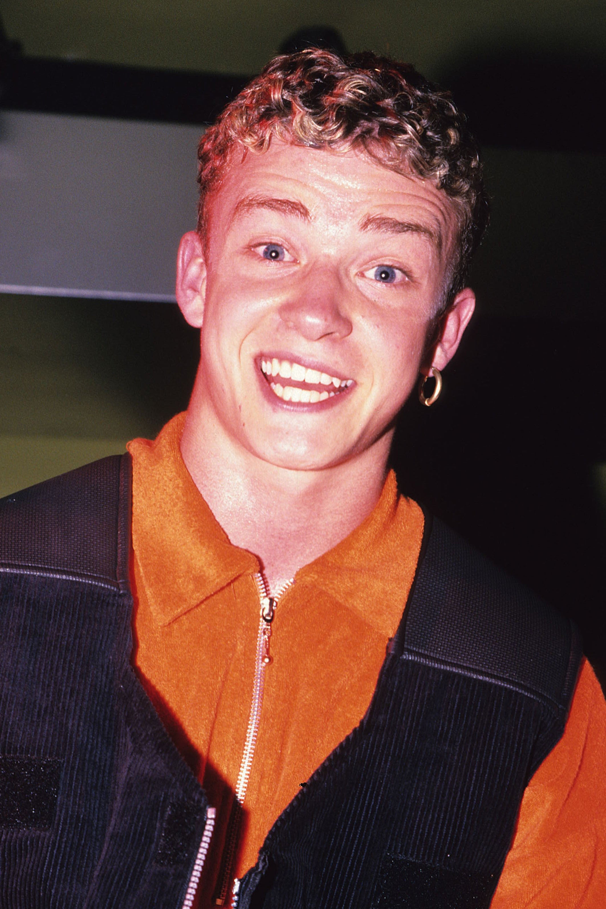 Person smiling widely, wearing a zip-up overgarment with a hoop earring