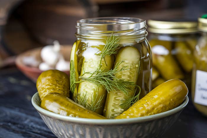 A jar of pickles with dill successful  a bowl, surrounded by escaped   pickles and ail  cloves
