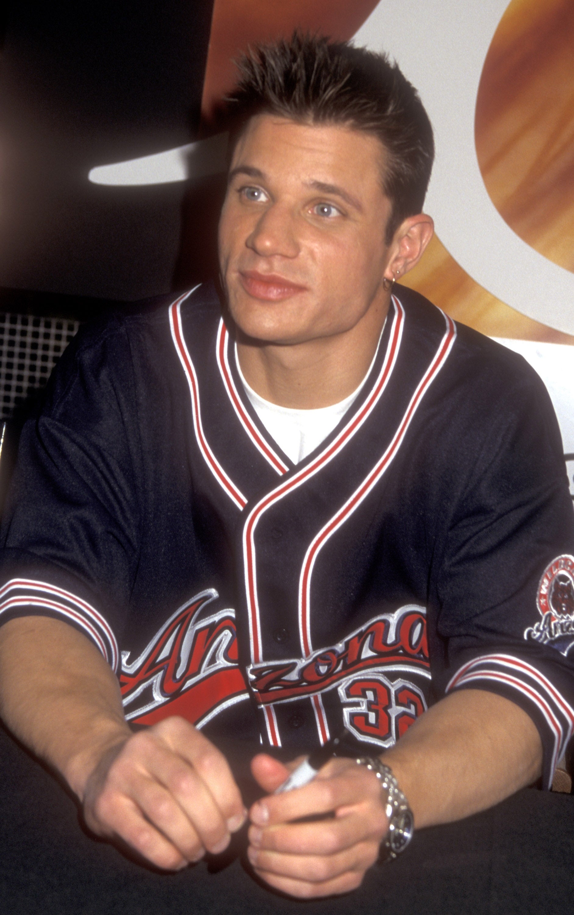 Person wearing a casual sports jersey with styled abbreviated hair, sitting astatine an autograph session