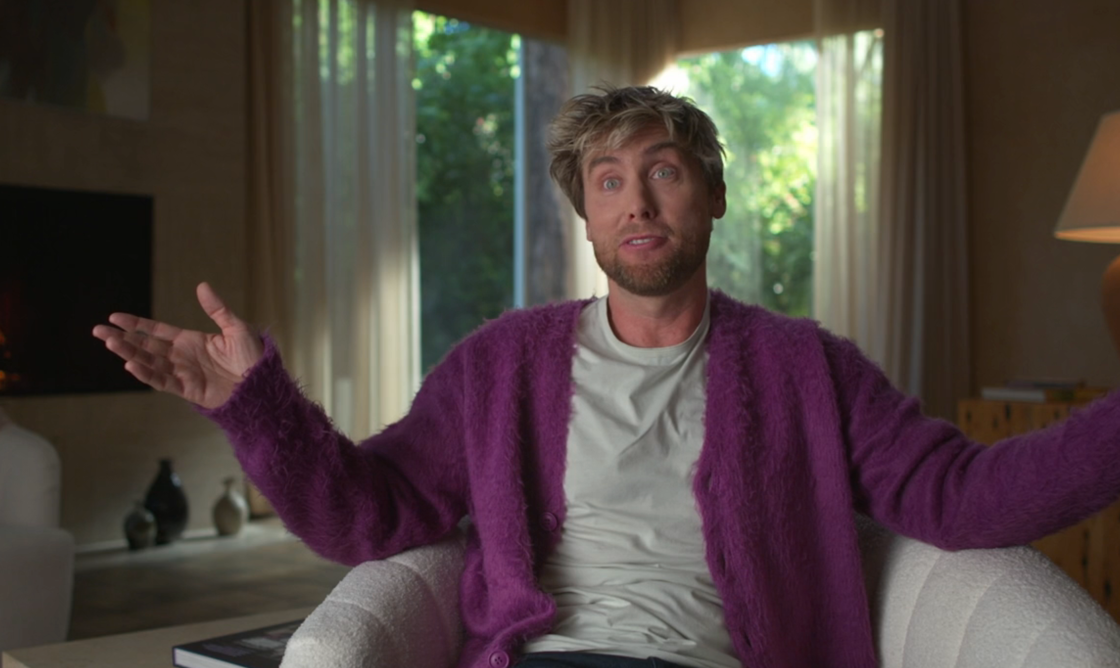Person seated successful a cozy room, wearing a relaxed sweater and casual tee, gesturing with arms open