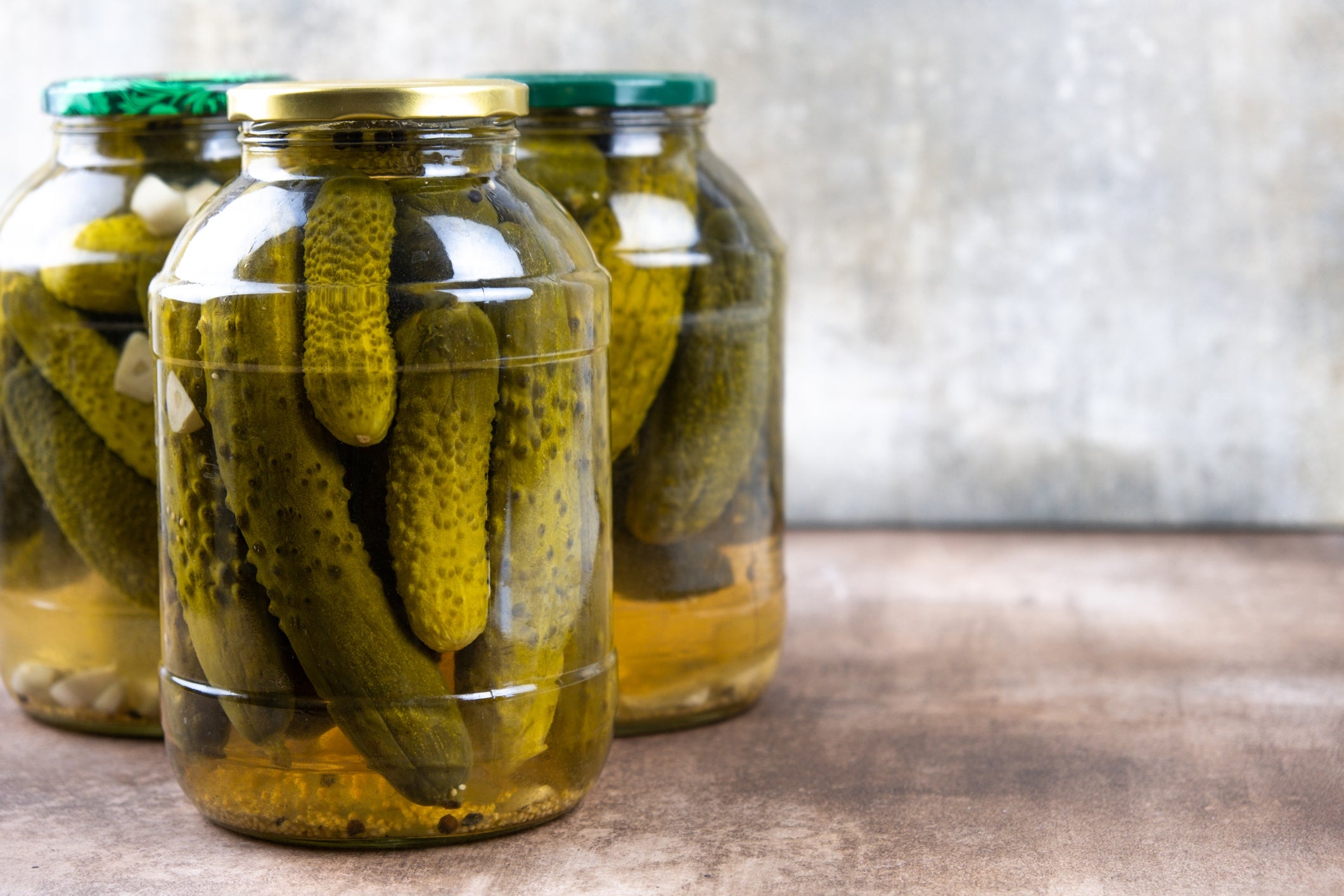 Three jars filled with pickles beryllium   connected  a woody  aboveground  against a plain background
