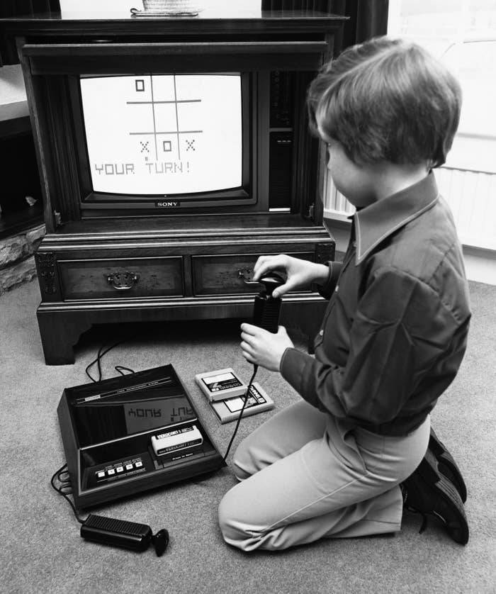 A child plays a tic-tac-toe video game on a vintage home console, holding a joystick in front of an old TV