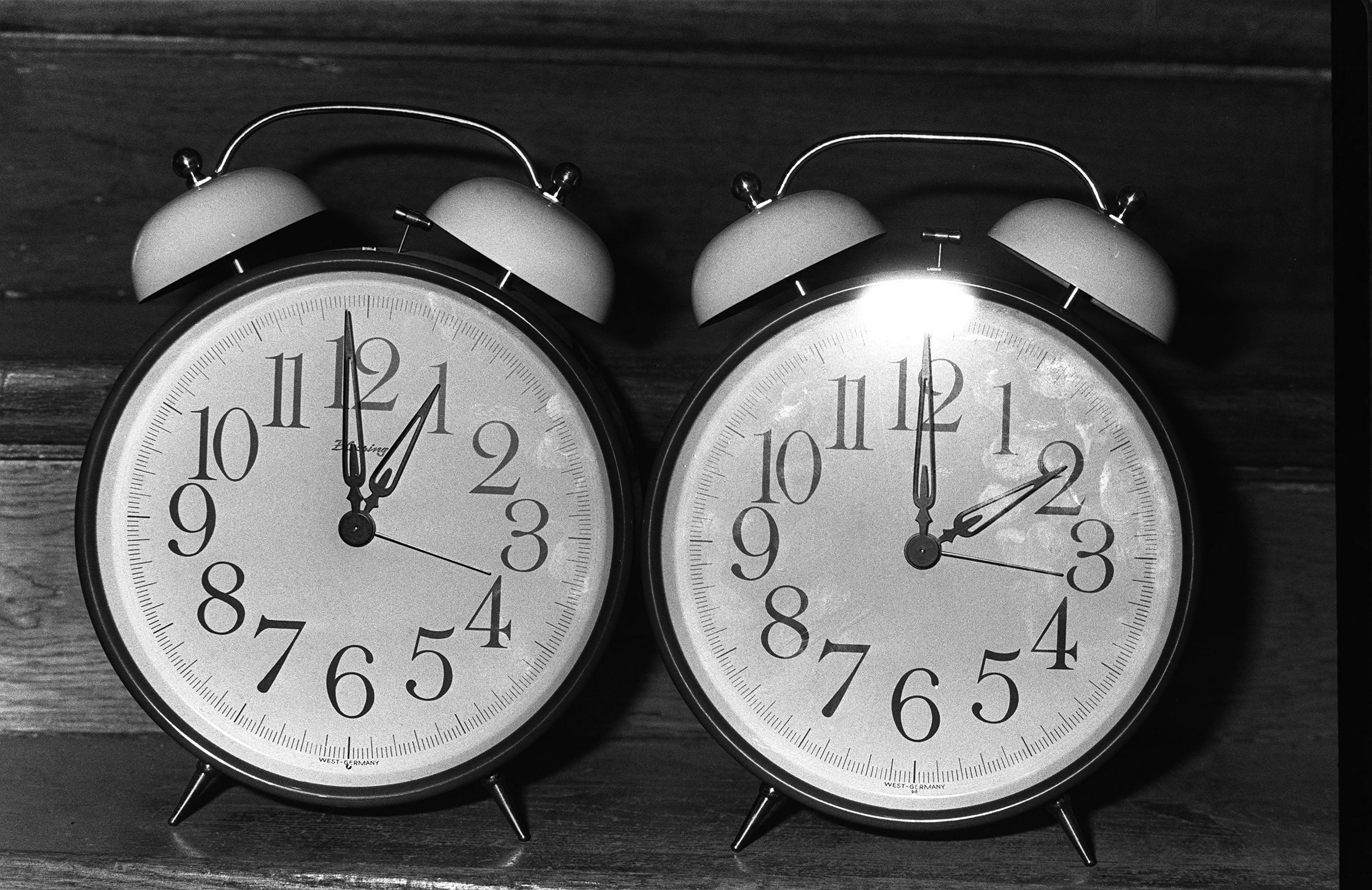 A classic analog alarm clock shows 10:09. It has two bells on top and is placed on a wooden surface