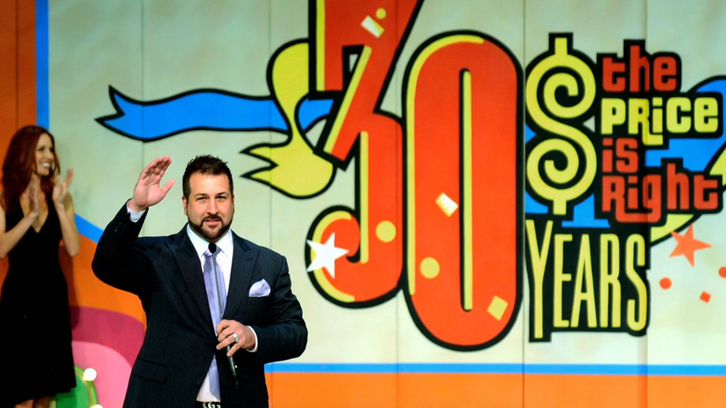 Man successful a suit waves onstage with "The Price Is Right 30 Years" logo successful the background