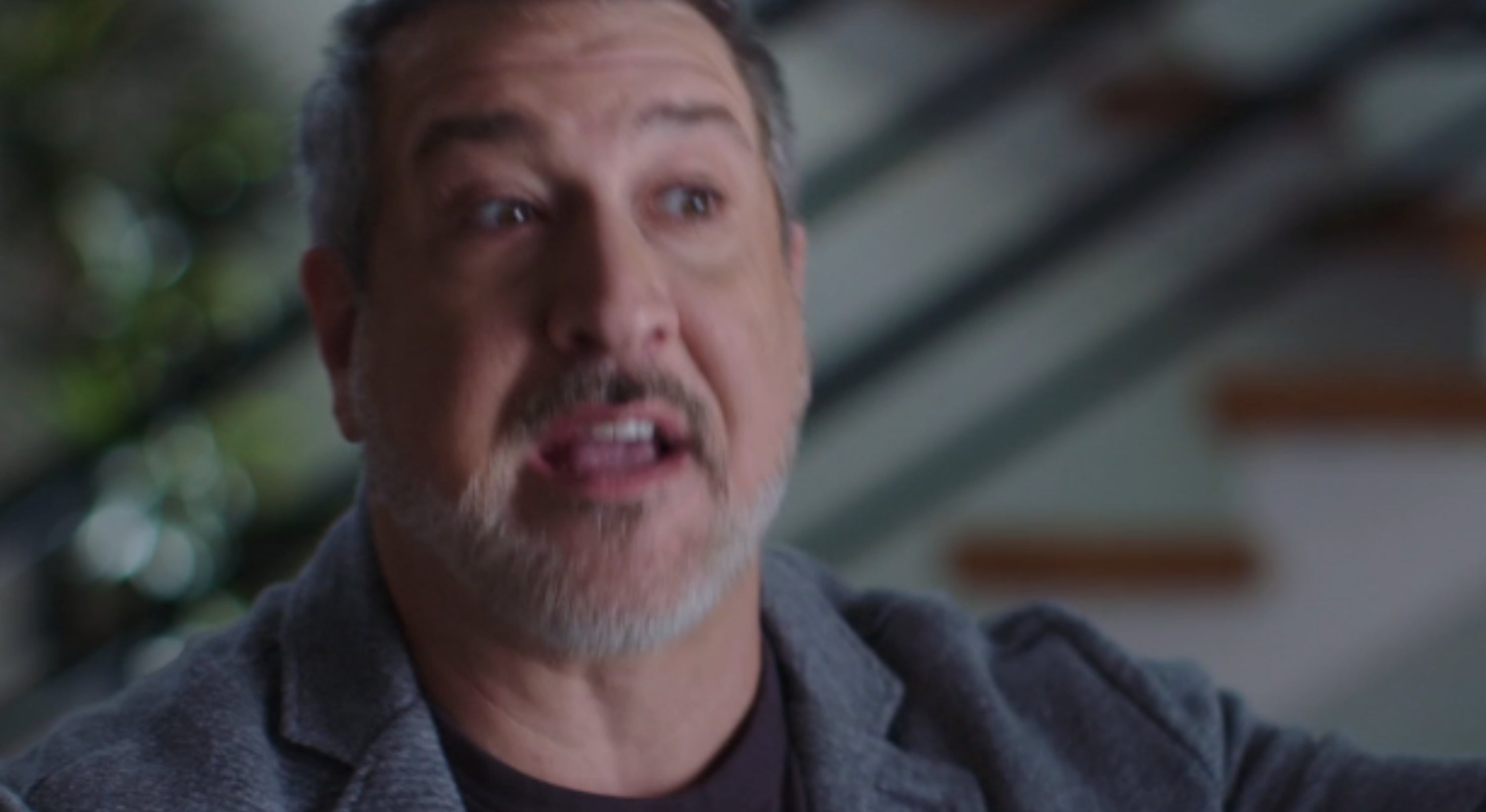 Person speaking successful an interrogation setting, wearing a blazer implicit a acheronian shirt. Background shows a staircase