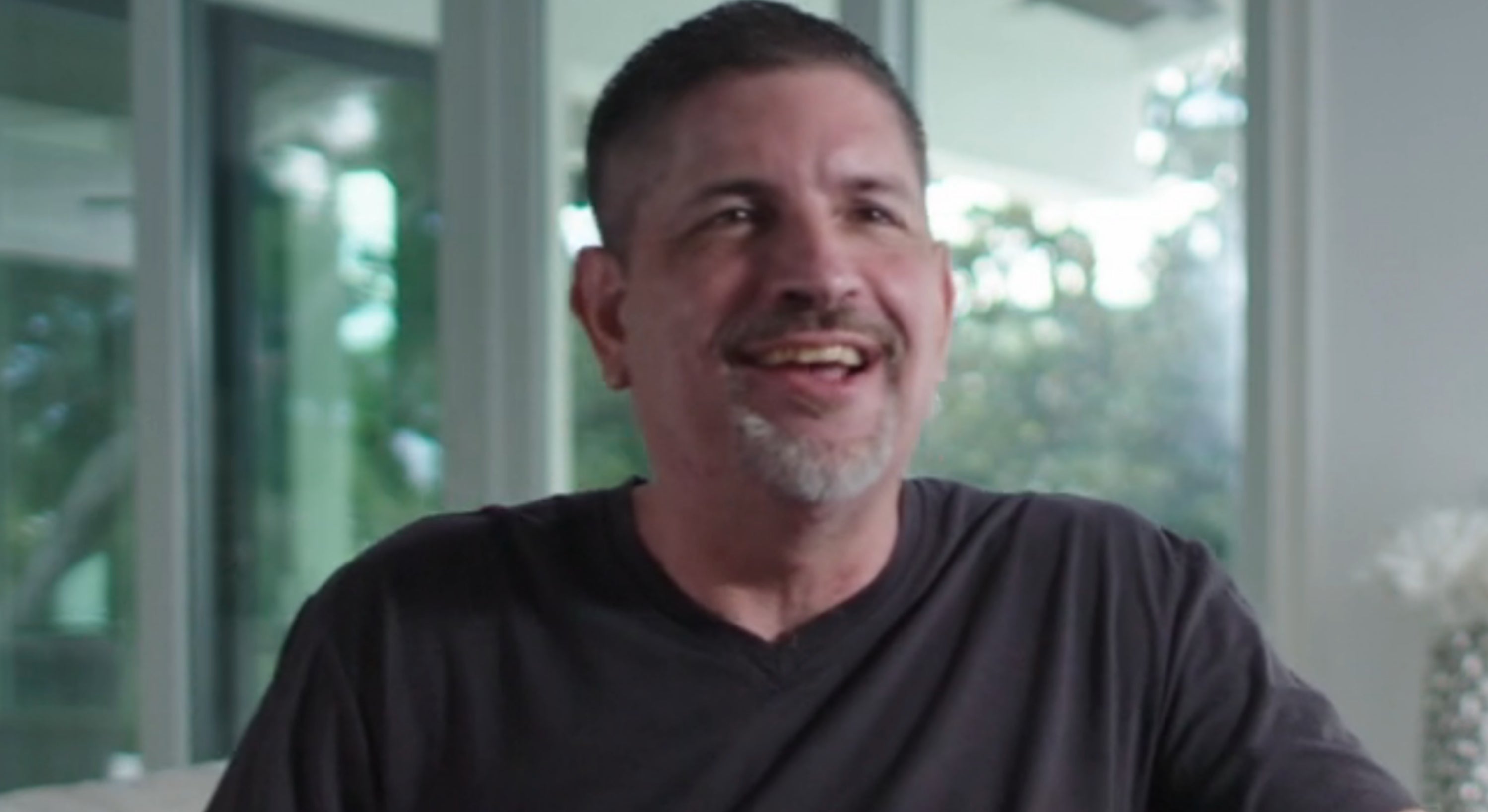 A idiosyncratic seated successful a modern location setting, smiling and wearing a casual t-shirt, with substance identifying them arsenic an archetypal subordinate of *NSYNC