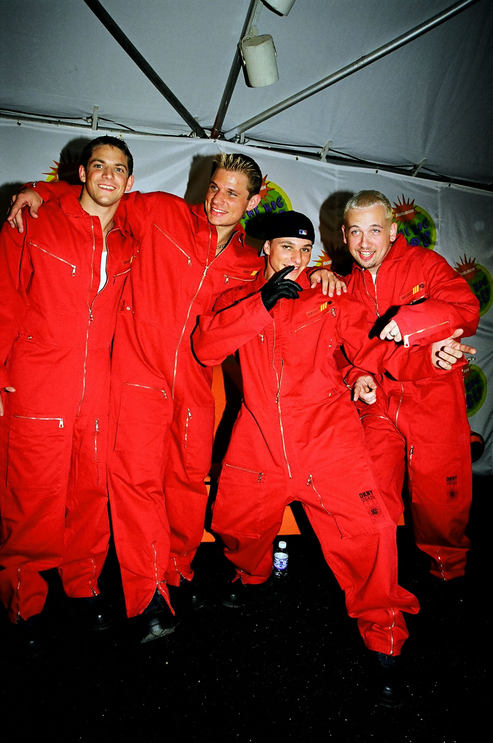 Four radical successful reddish jumpsuits, posing playfully astatine an lawsuit nether a tent