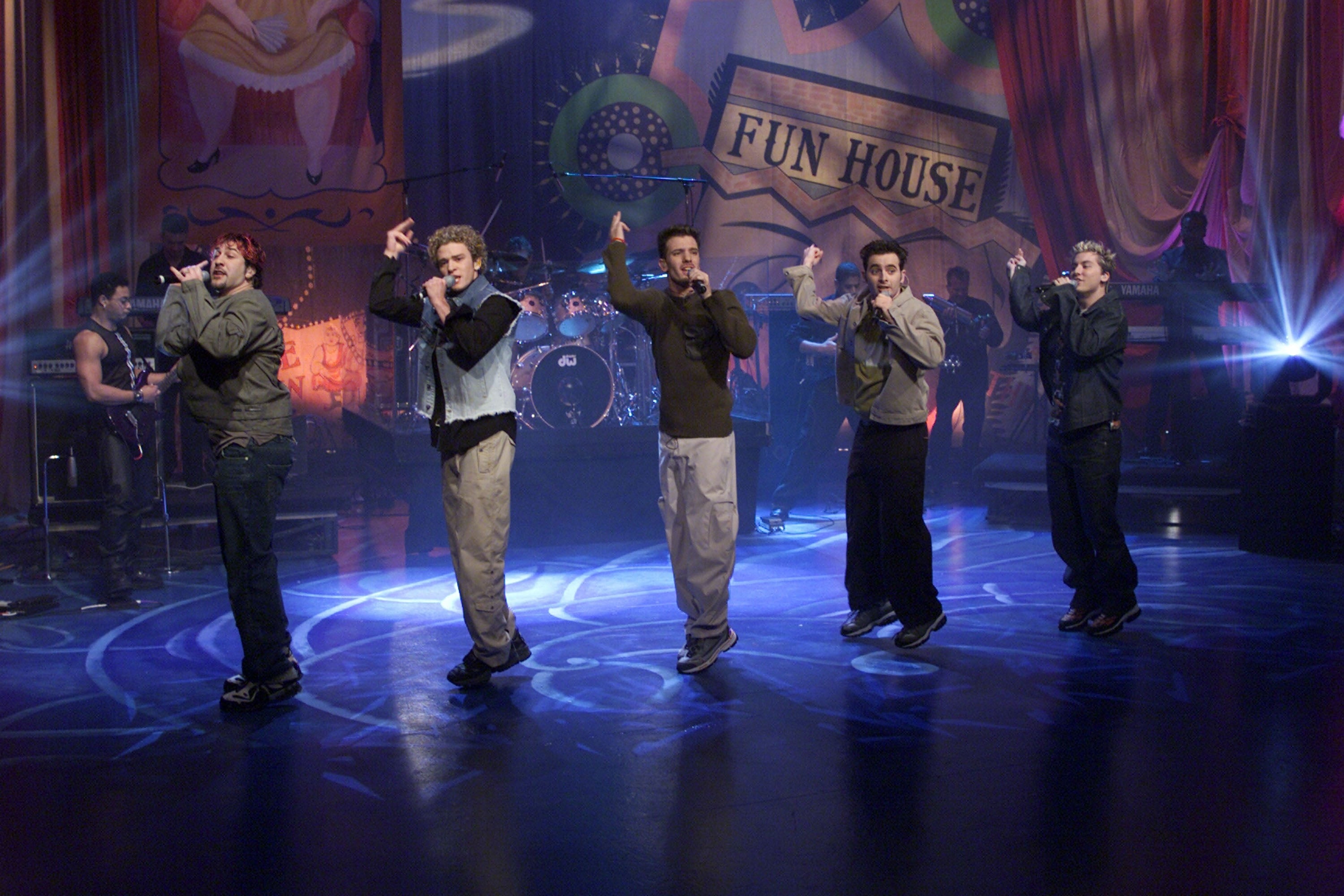 A lad set performs connected a signifier with a "Fun House" backdrop, wearing casual, coordinated outfits and striking creation poses