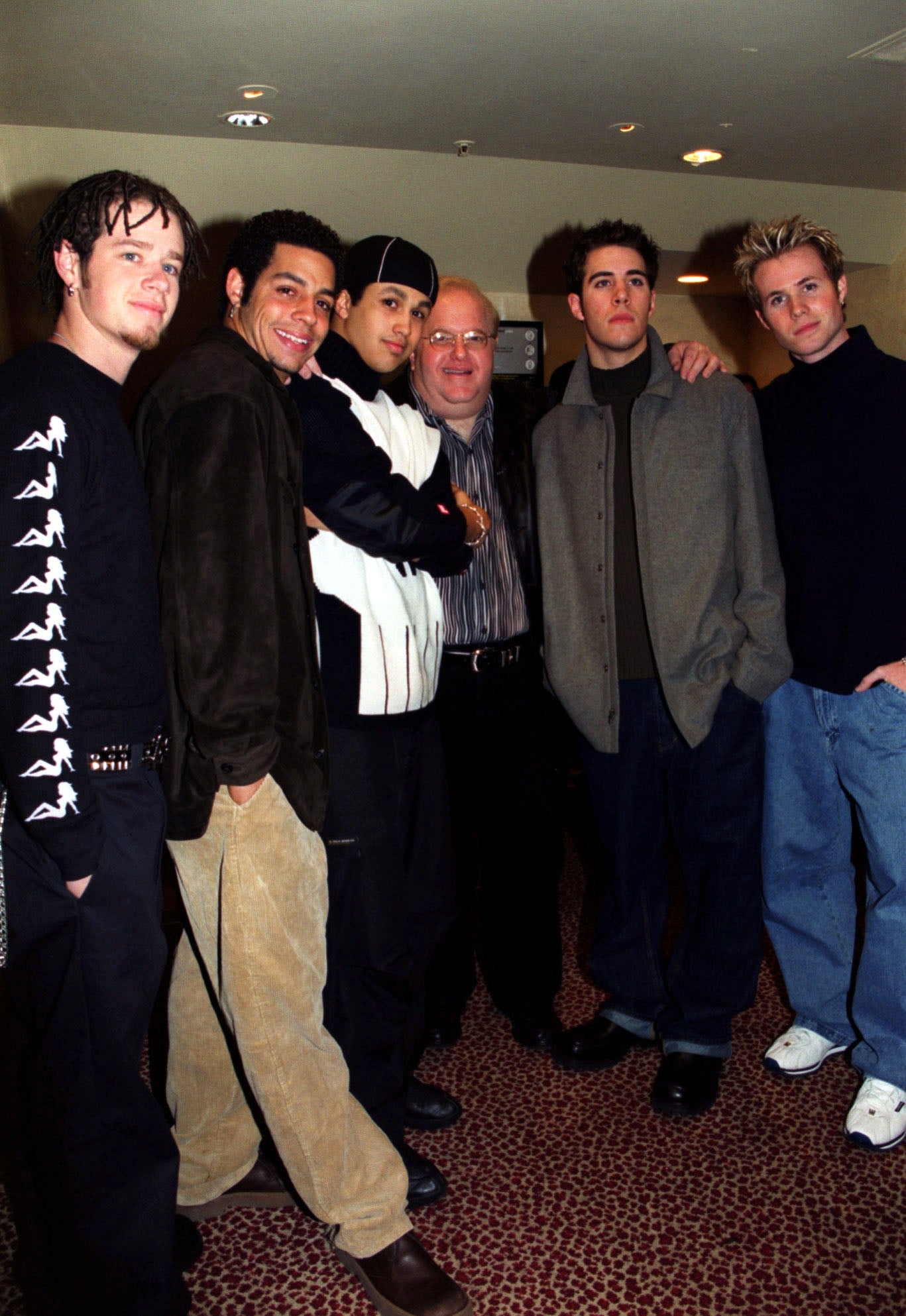 Group of six men posing together, immoderate successful casual streetwear and immoderate successful relaxed suits, connected a patterned carpet astatine a nationalist event