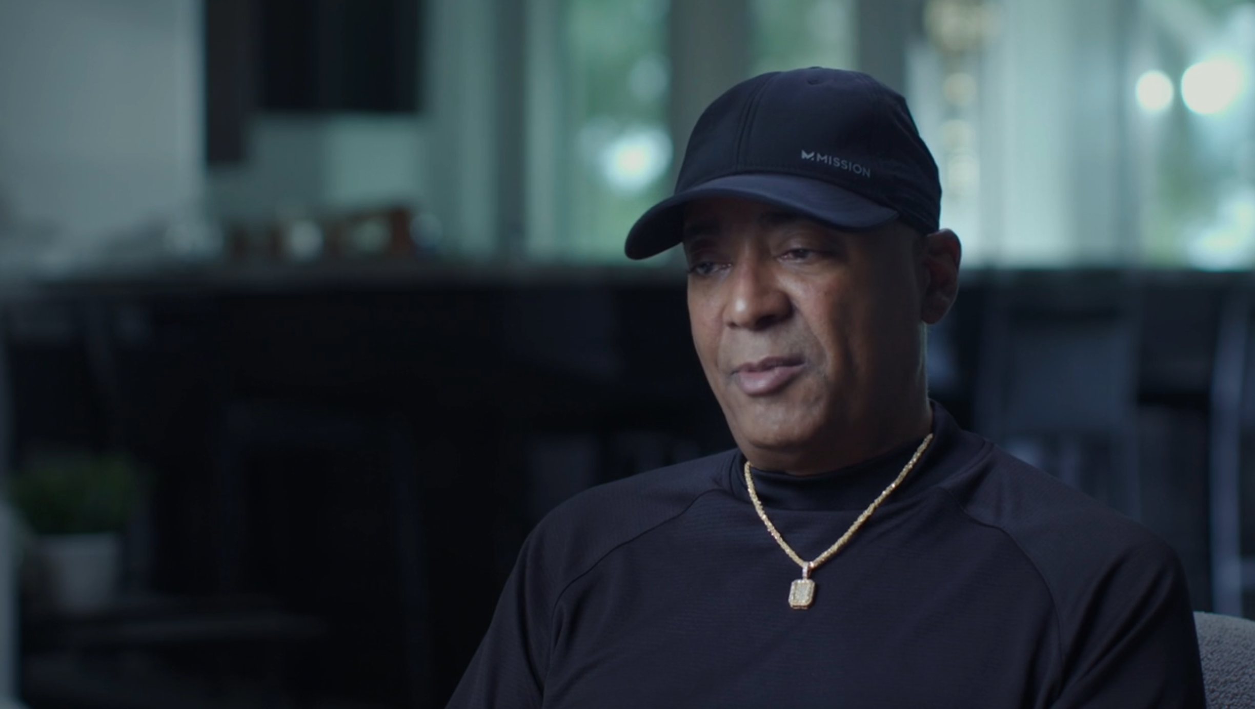 A idiosyncratic successful a achromatic headdress and shirt, wearing a golden chain, sits successful a dimly lit room