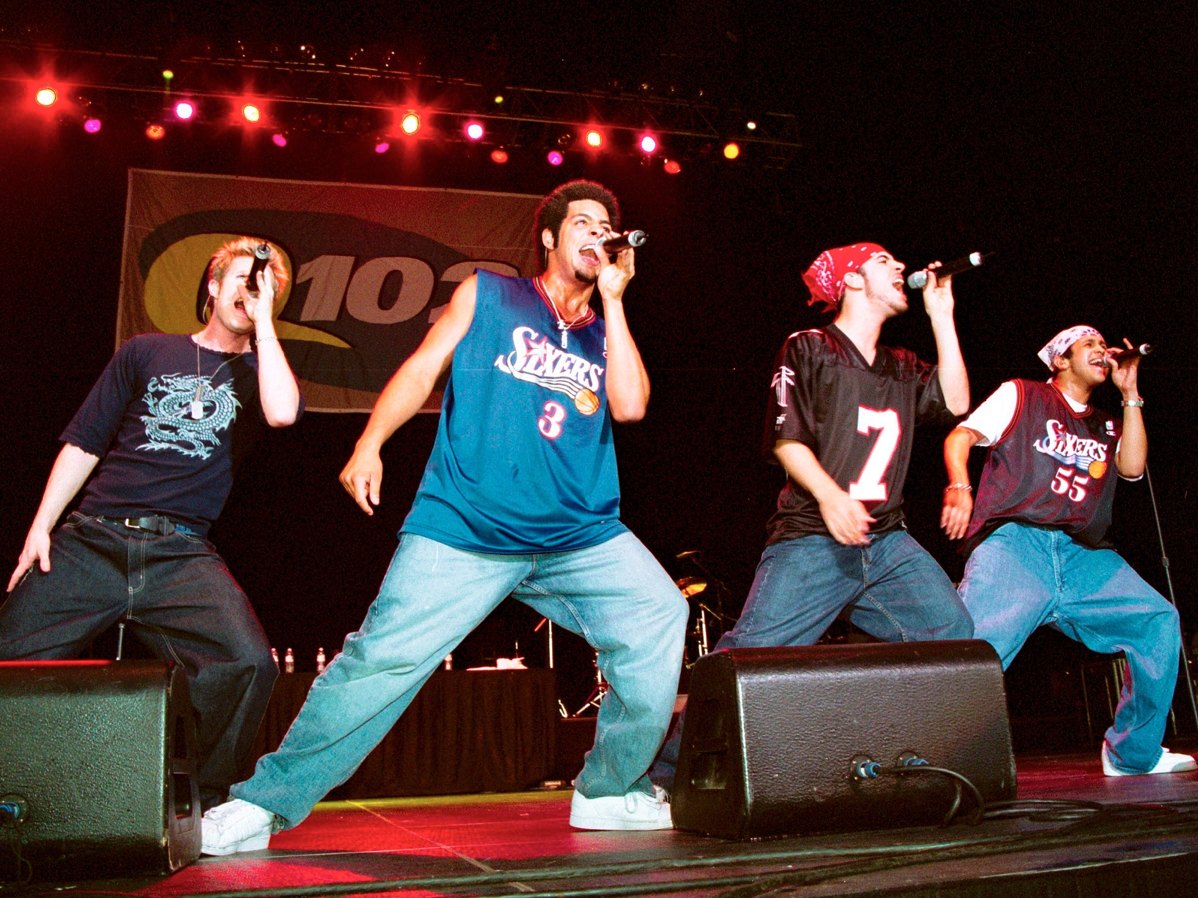 A euphony radical performs energetically connected stage, each subordinate wearing casual outfits and jerseys, nether colorful signifier lights