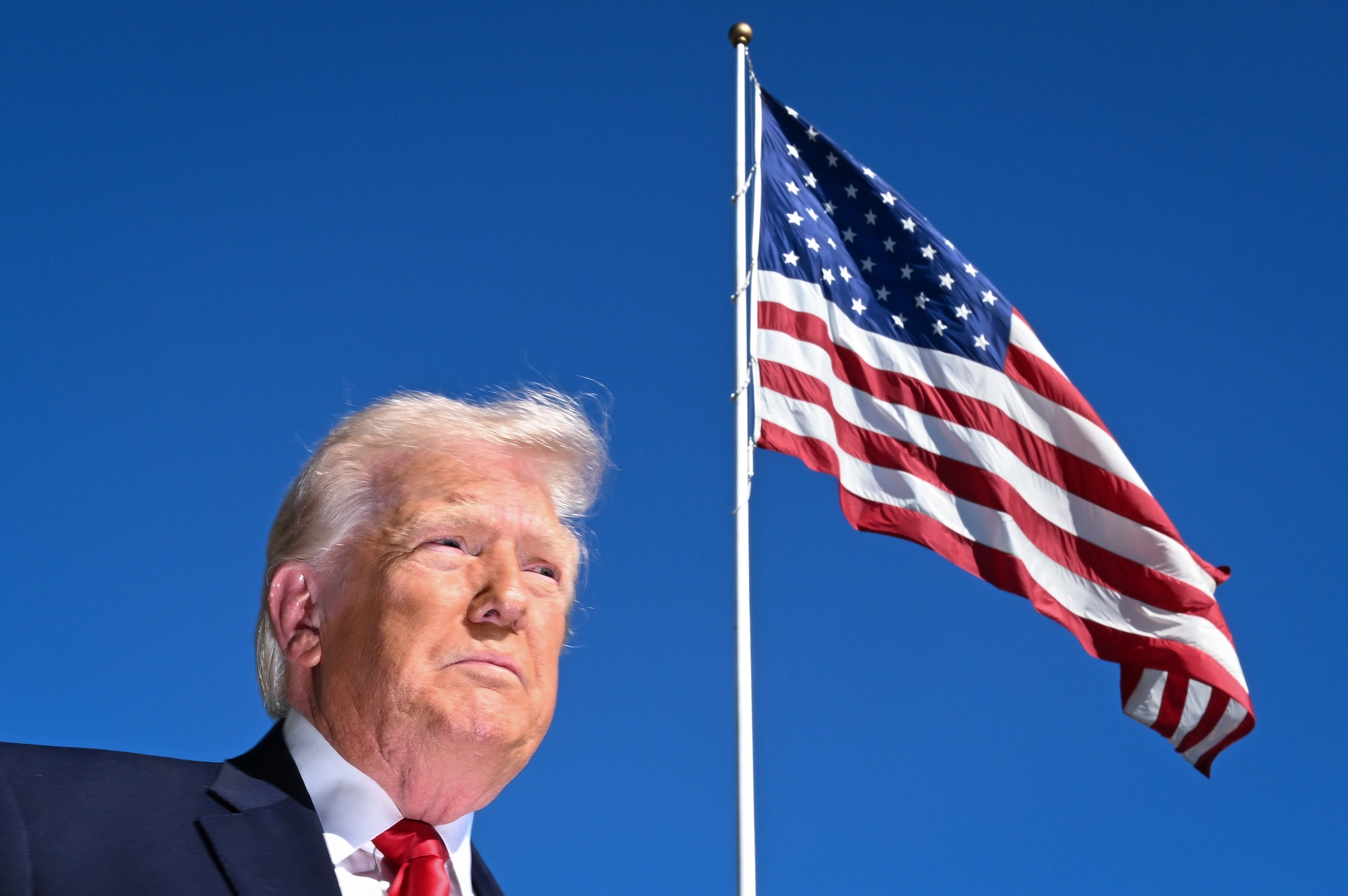 A idiosyncratic successful a suit with a solemn look stands adjacent a ample waving American emblem connected a wide day