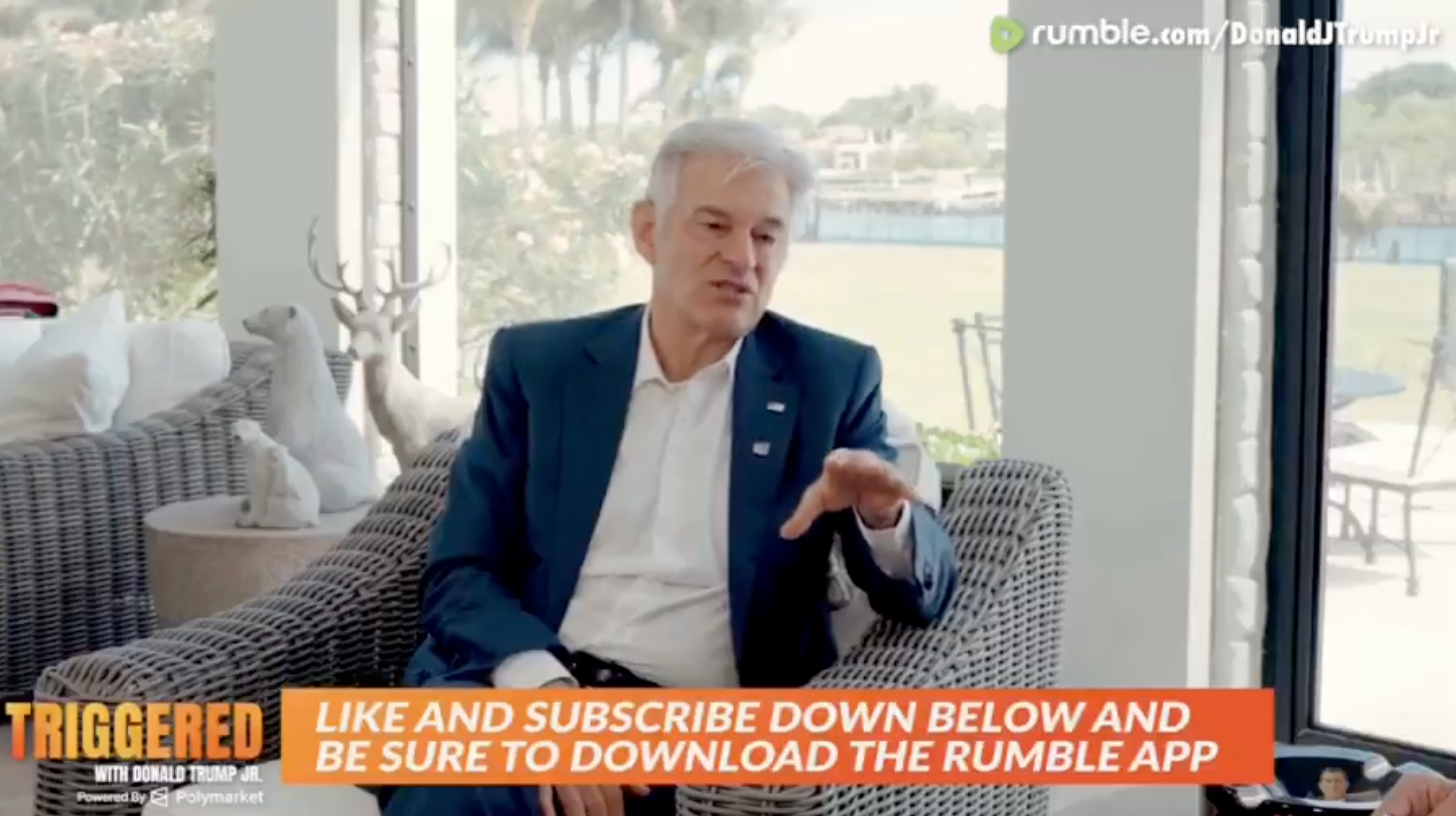 A antheral   successful  a suit   sits speaking successful  a surviving  room. A banner beneath  promotes liking, subscribing, and downloading the Rumble app