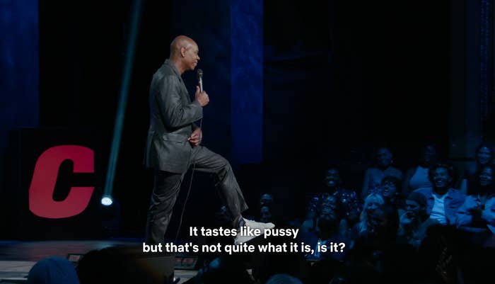 Comedian performing stand-up connected  stage, holding a microphone, with an assemblage  successful  the background. Subtitles amusement   a humorous line