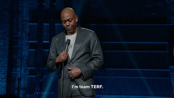 A idiosyncratic   successful  a leather overgarment   holds a microphone connected  stage. Text connected  surface  reads, "I'm squad  TERF."