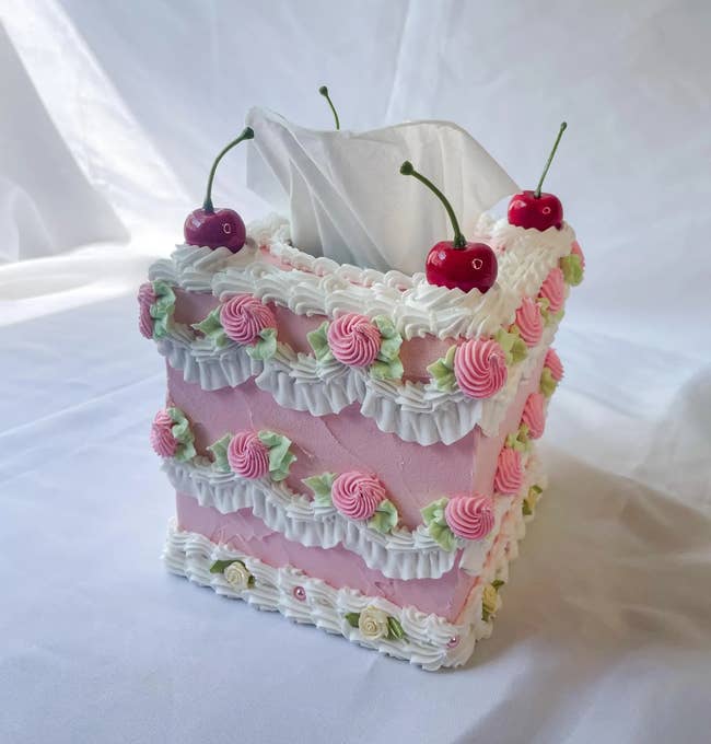 Tissue container designed to look similar a decorative cake, adorned with faux icing and cherries connected top