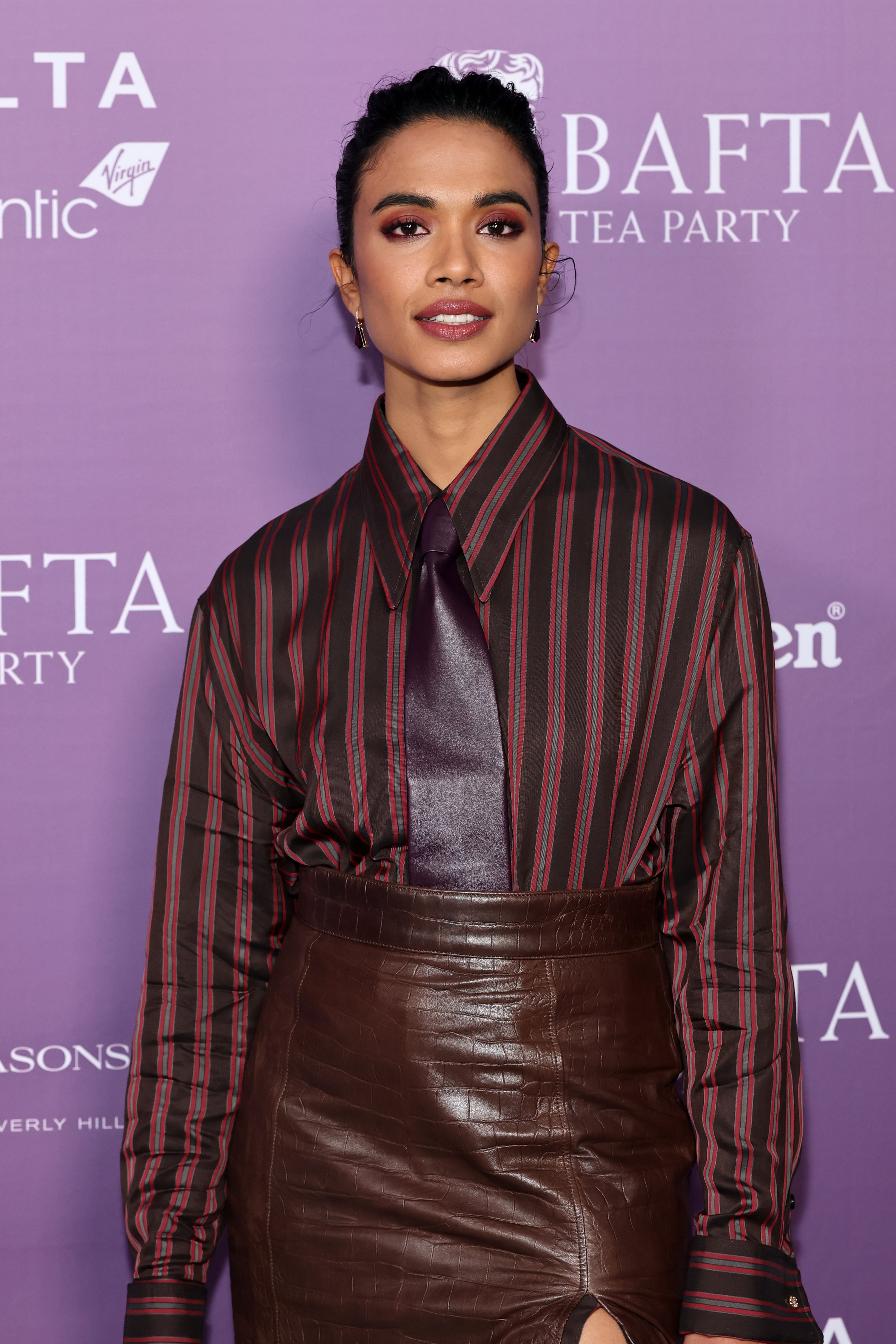 Person wearing a striped garment  with an oversized necktie  and leather skirt astatine  a BAFTA event, posing for photos