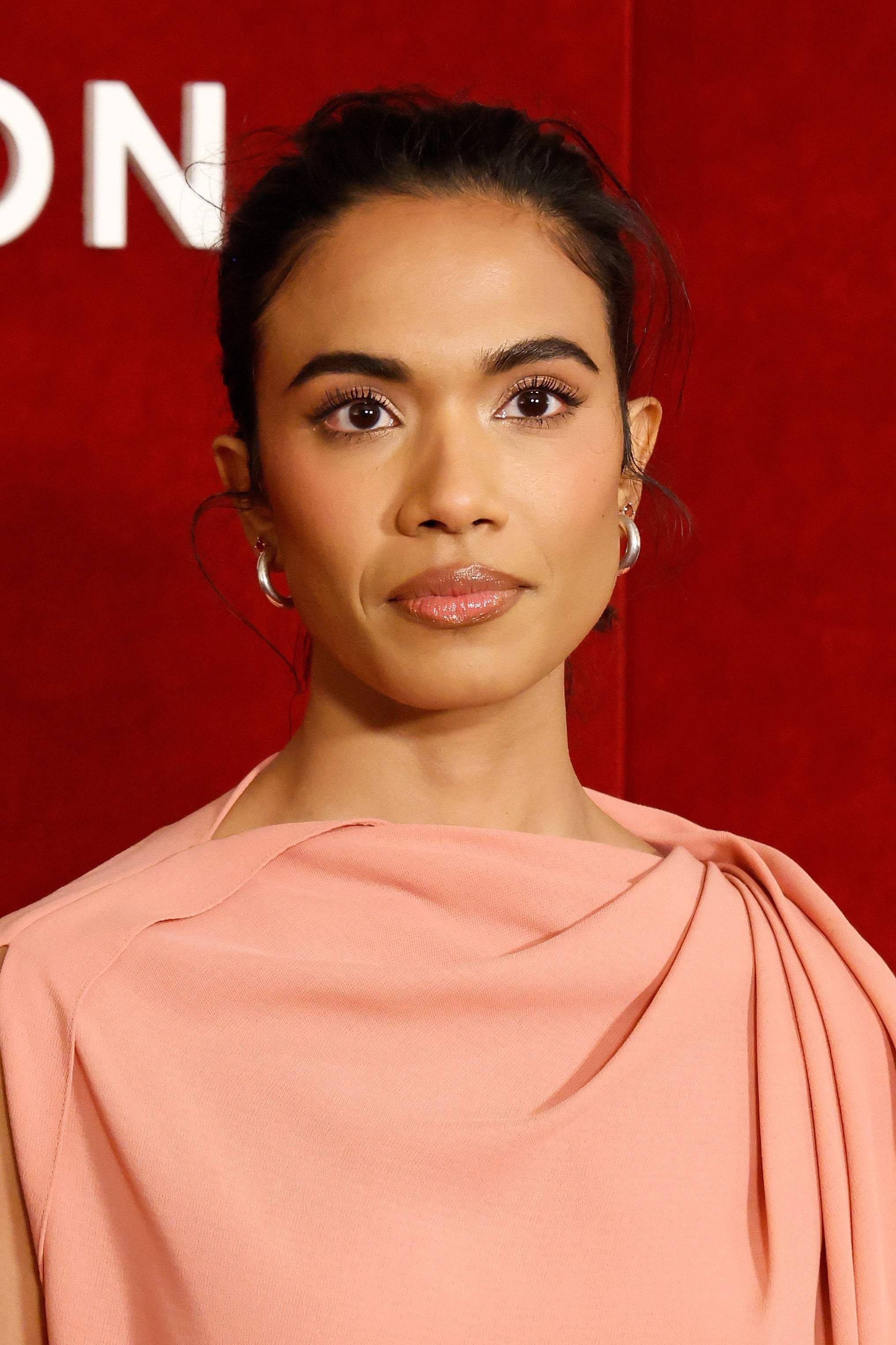 Person poses connected  a reddish  carpet successful  an elegant draped dress, featuring minimal constitution  and subtle earrings
