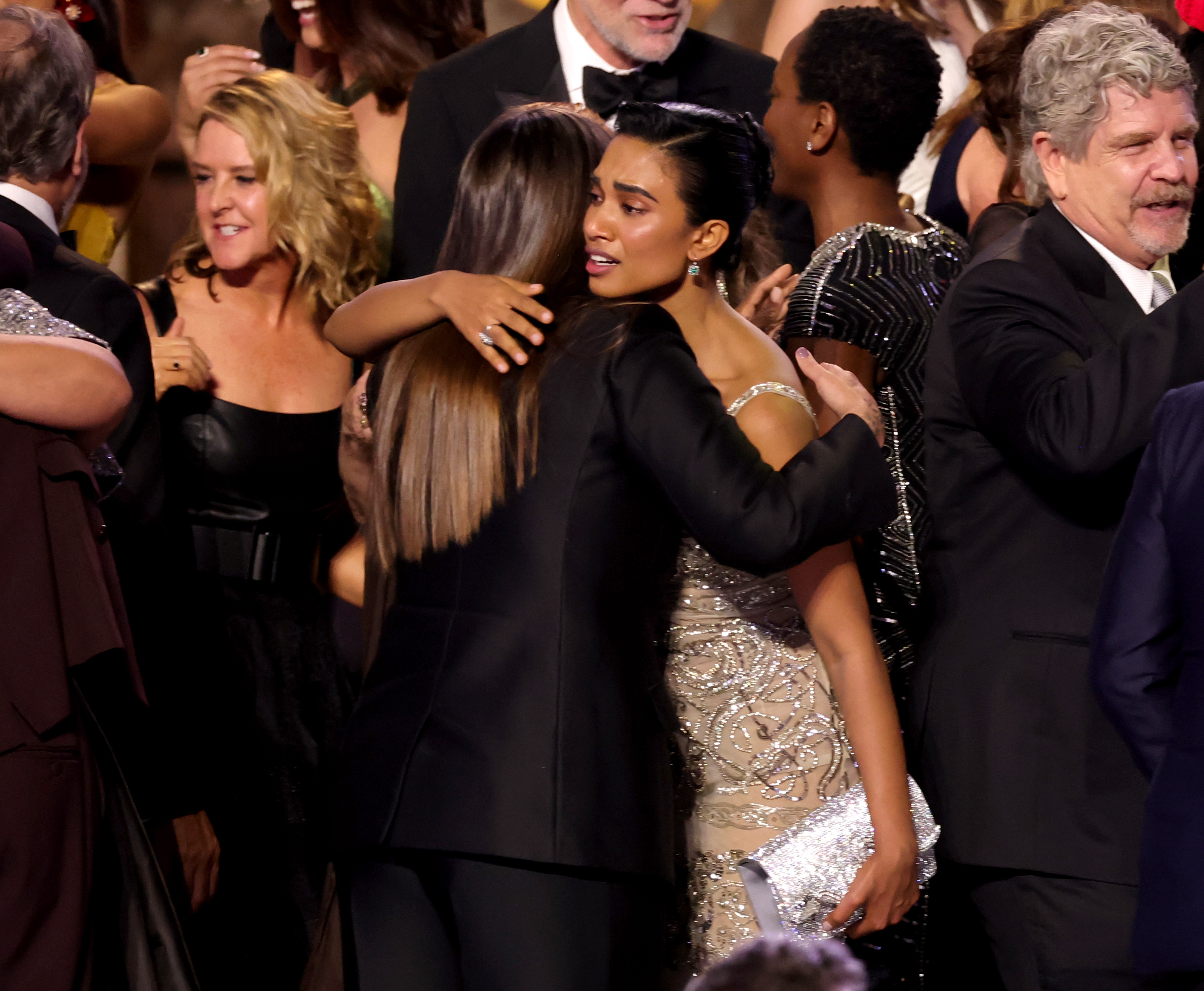 People hugging and celebrating astatine  a ceremonial  event, with 1  idiosyncratic  wearing a sequined gown holding a metallic  clutch