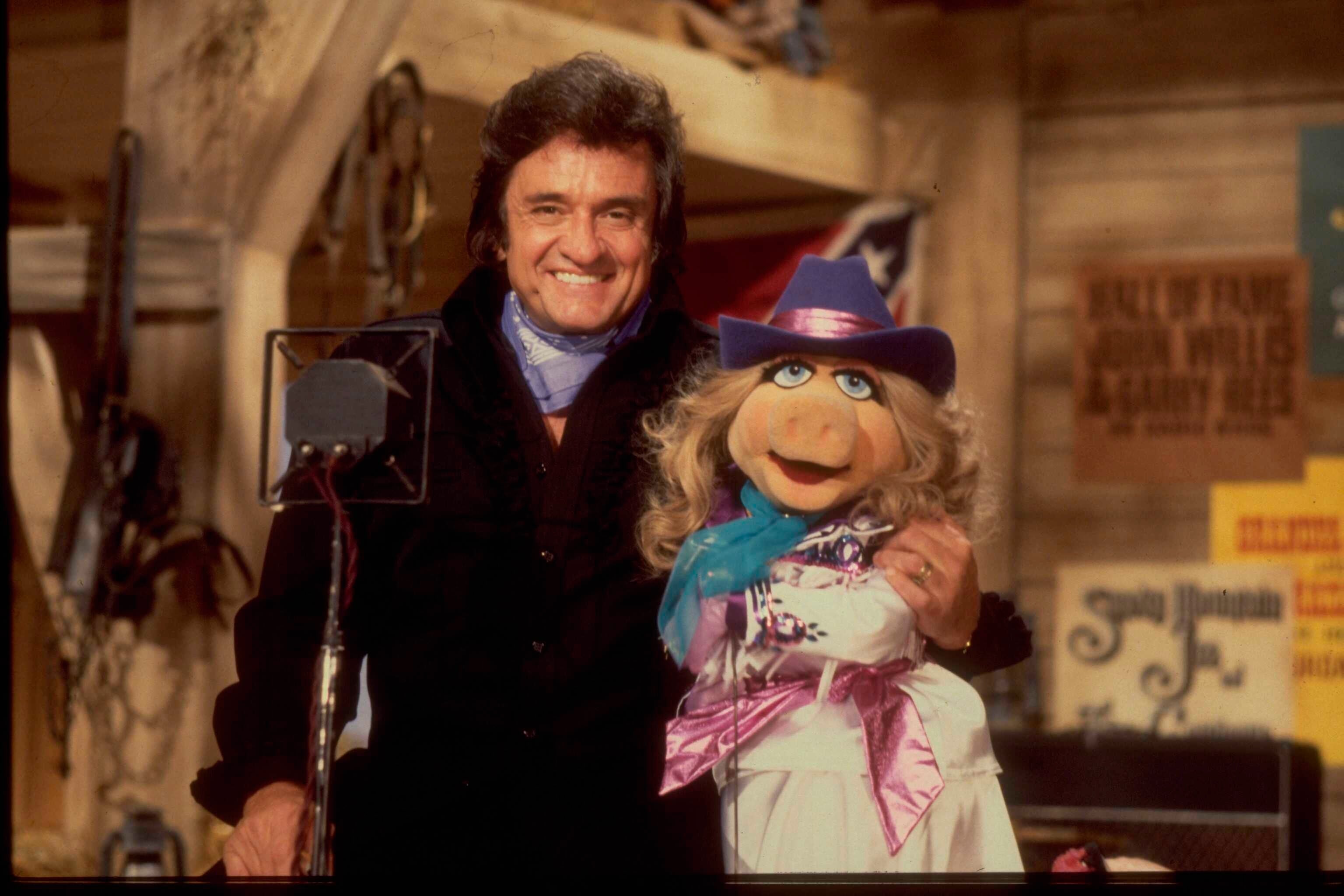 A impermanent  smiles adjacent  to a celebrated  puppet successful  a rustic set, some  dressed successful  stylish, western-themed outfits, including hats and scarves