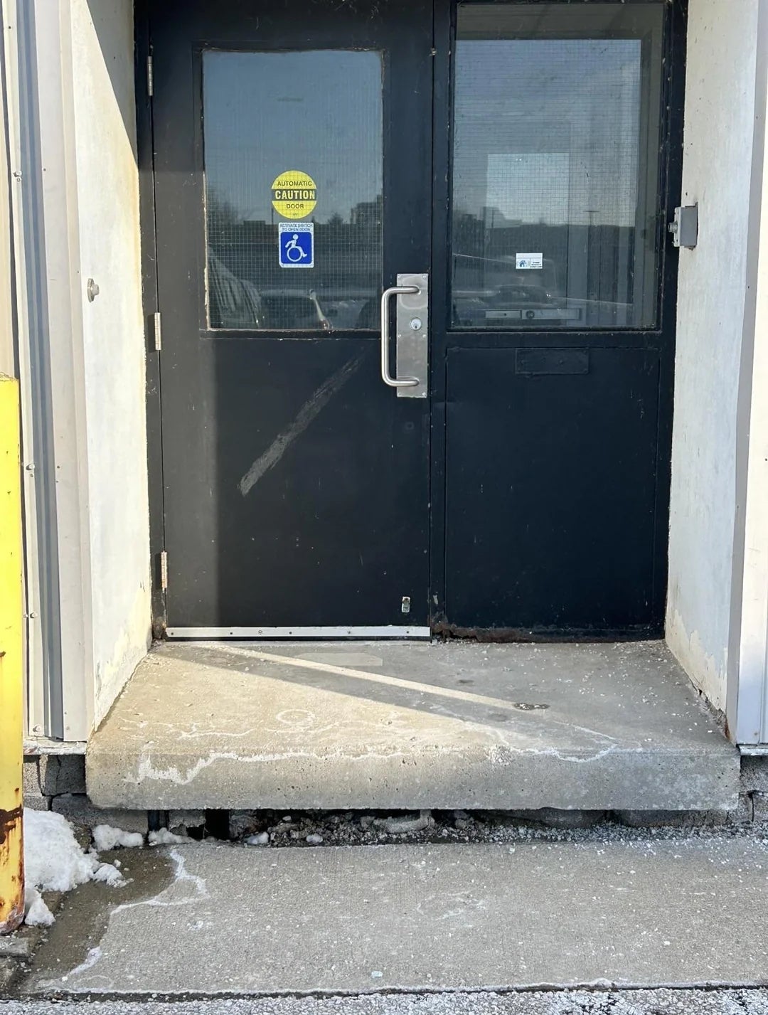 A doorway  with a step, ADA handicap motion   visible, but nary  ramp for wheelchair access