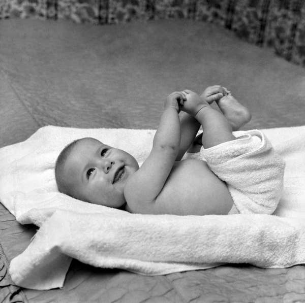 Baby lying on a towel, smiling and holding their feet, with a joyful expression