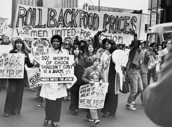 Protest with people holding signs demanding lower food prices, including a banner saying "Roll Back Food Prices."