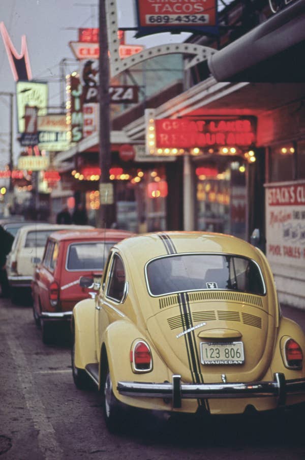 Vintage cars lined up on a retro street with neon signs and diners, evoking a nostalgic, classic Americana vibe