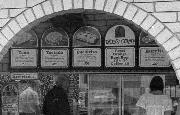 Vintage Taco Bell menu showing prices for tacos, tostadas, enchiritos, and burritos along with drinks like Pepsi, root beer, and coffee