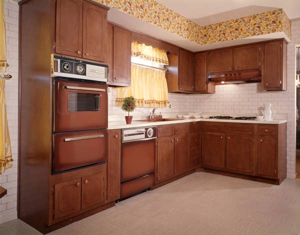 Retro kitchen with wooden cabinets, vintage appliances, floral wallpaper border, and a small plant on the counter