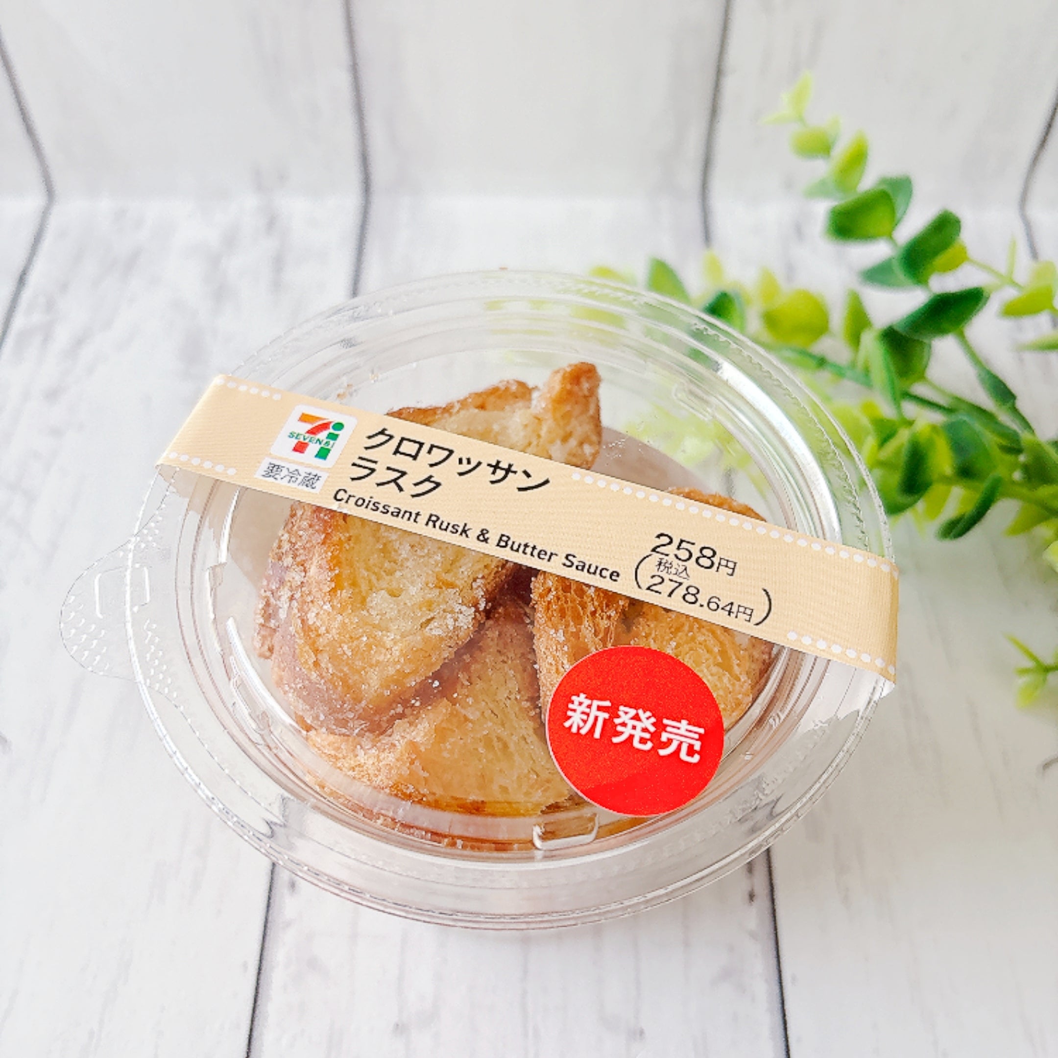 セブン-イレブンの「クロワッサンラスク」プラスチック容器に入ったクロワッサンラスク。新発売のシール付き。価格表示あり。