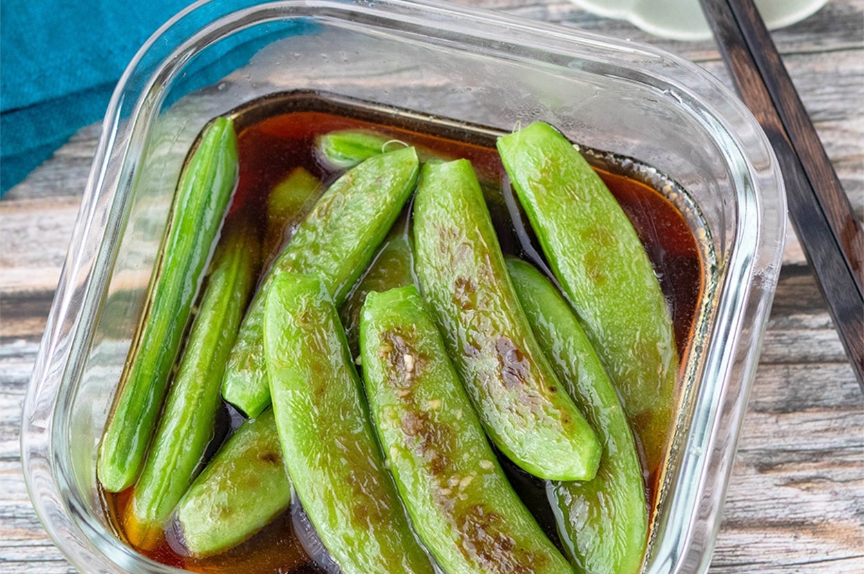 ガラスの容器に入った調理済みのインゲン豆が、醤油ベースの液体に浸されています。隣に箸があります。