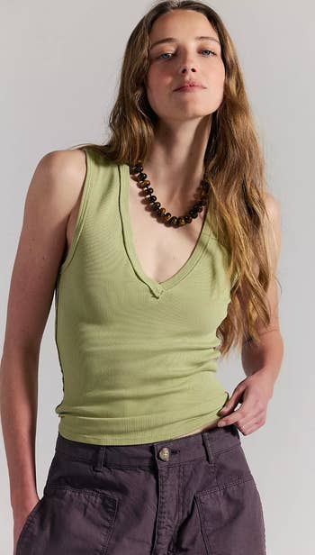 Person in a sleeveless ribbed V-neck top and cargo pants, wearing a beaded necklace, posing confidently