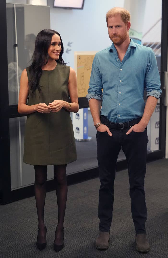 A mates  stands together; the pistillate   successful  a sleeveless formal  and the antheral   successful  a casual button-up garment  and jeans. They are indoors