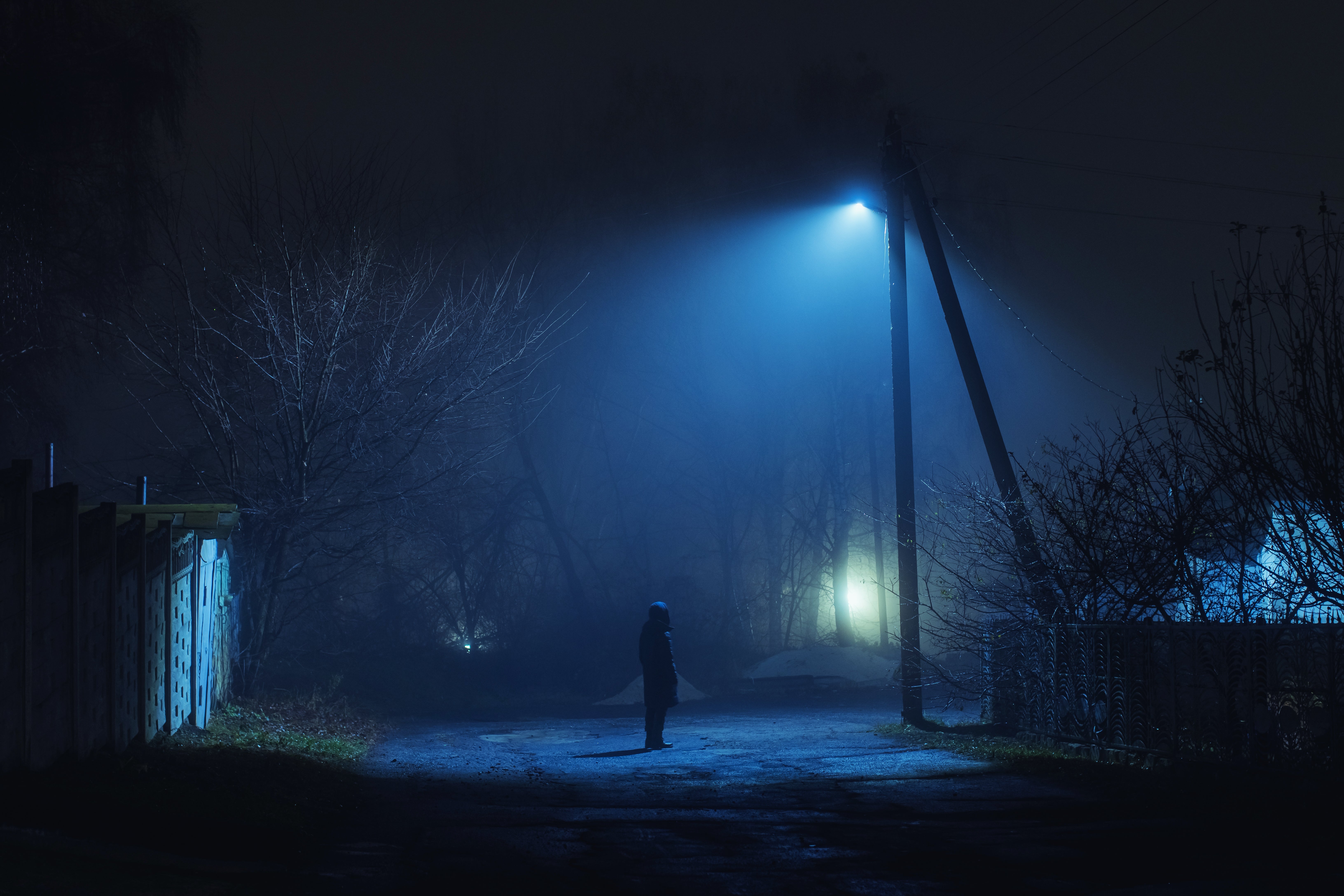 A solitary figure stands under a streetlight on a quiet, misty night, creating a mysterious and contemplative atmosphere