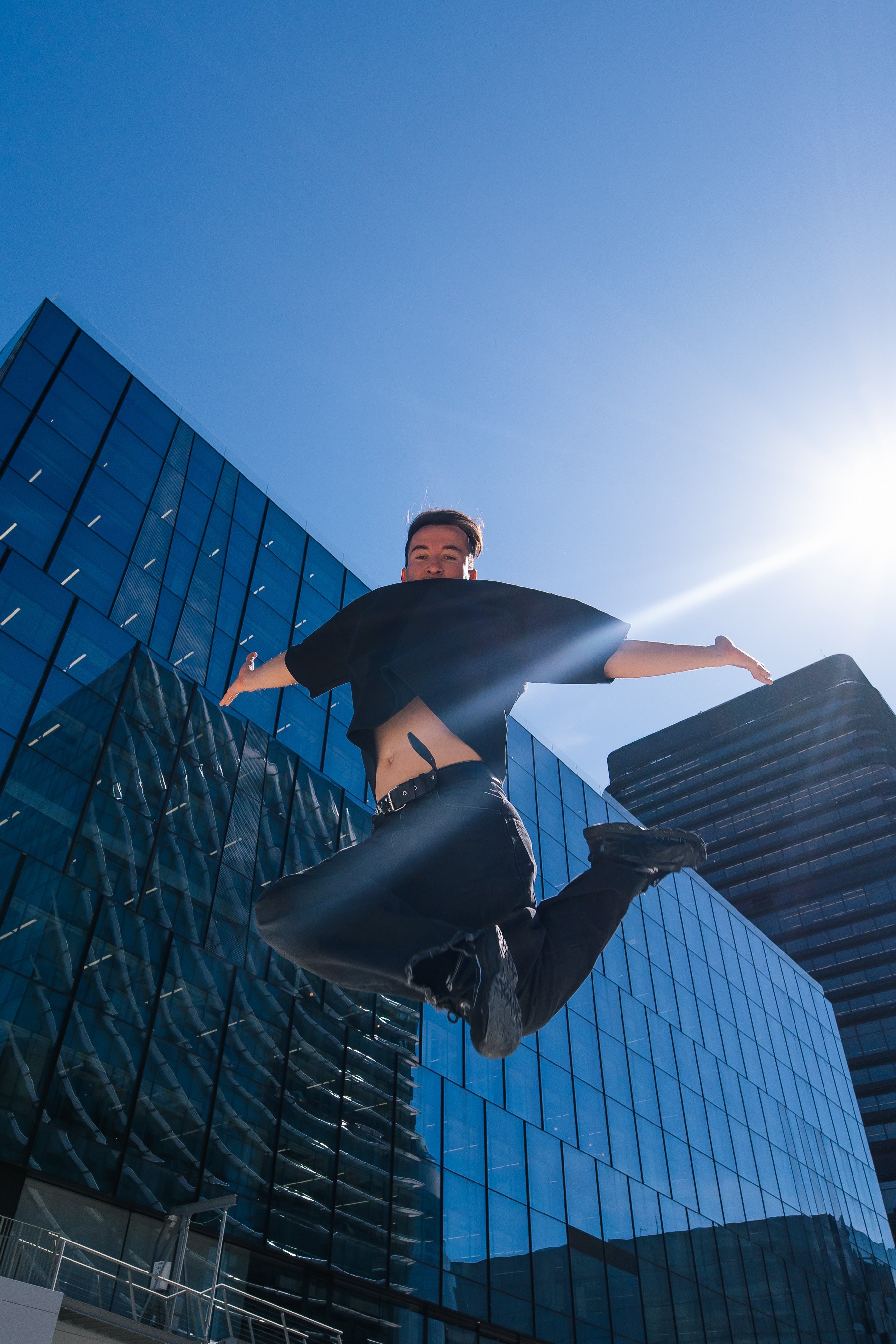 A person leaps energetically in front of modern glass buildings under a bright sky