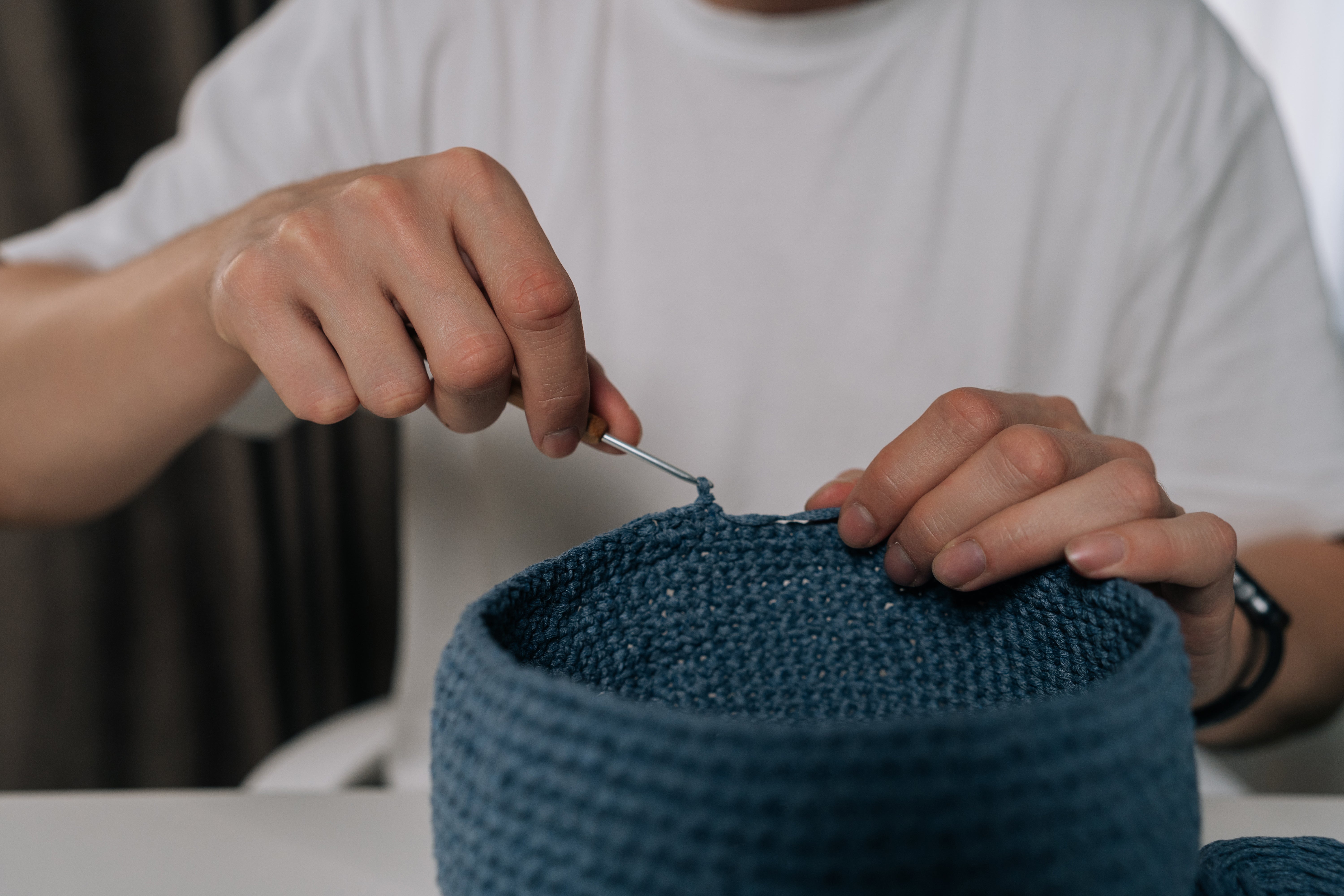 Person crocheting with a hook, working on a round basket. Close-up of hands focusing on the intricate needlework