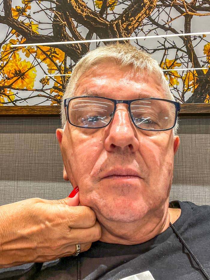 Person with glasses holds their chin thoughtfully in front of an artwork depicting tree branches