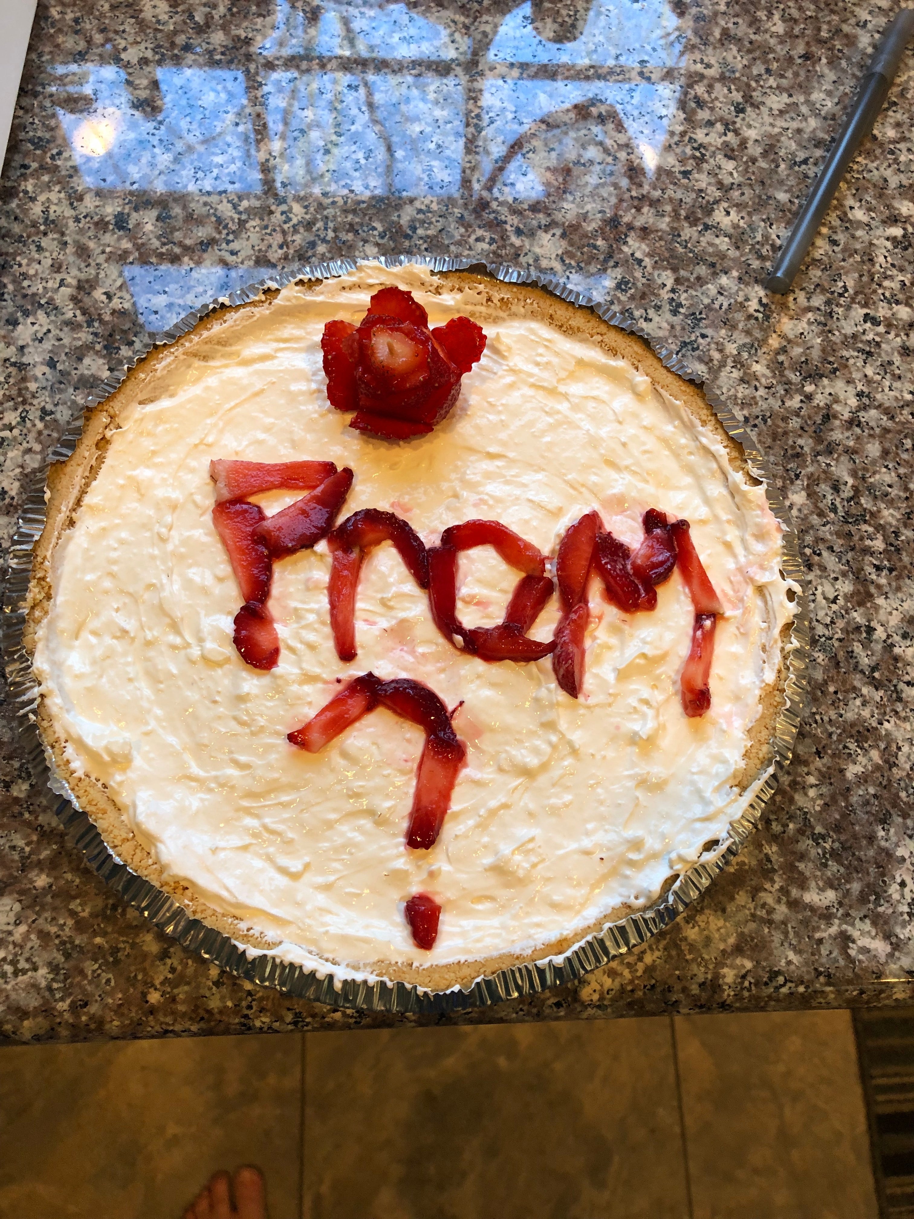 Pie with "Prom?" written in strawberry slices on a crumb crust, topped with a strawberry rose