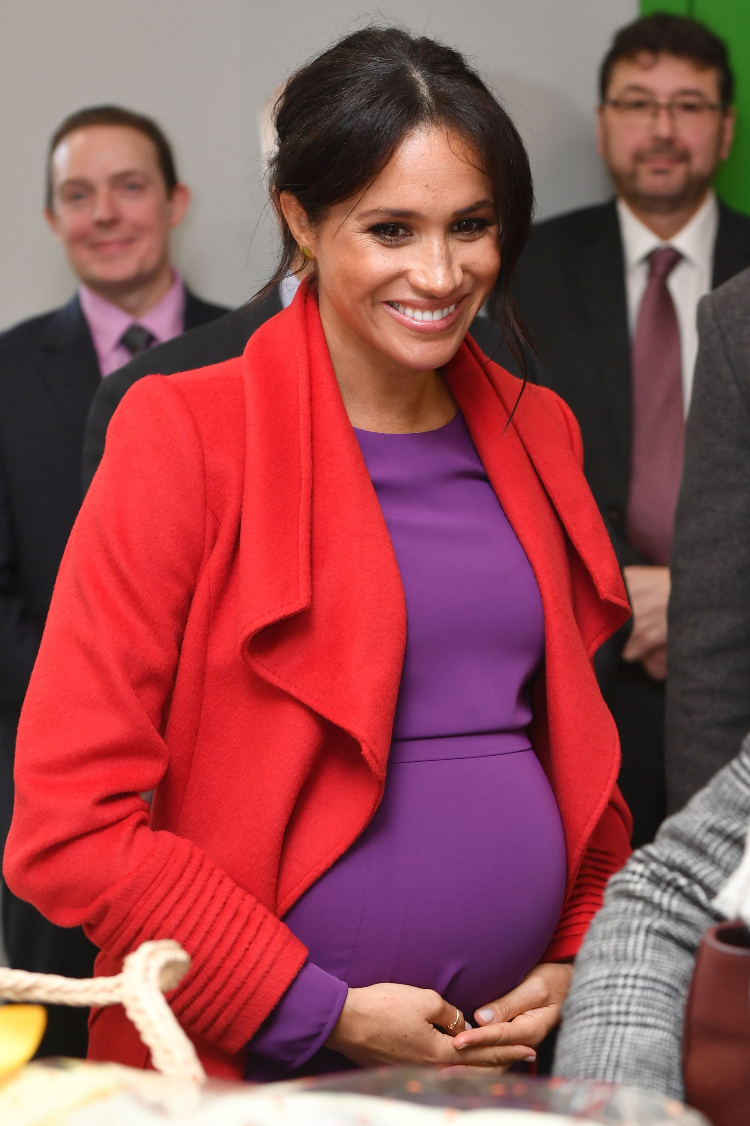 Person successful elegant attire holding their babe bump, smiling, surrounded by people